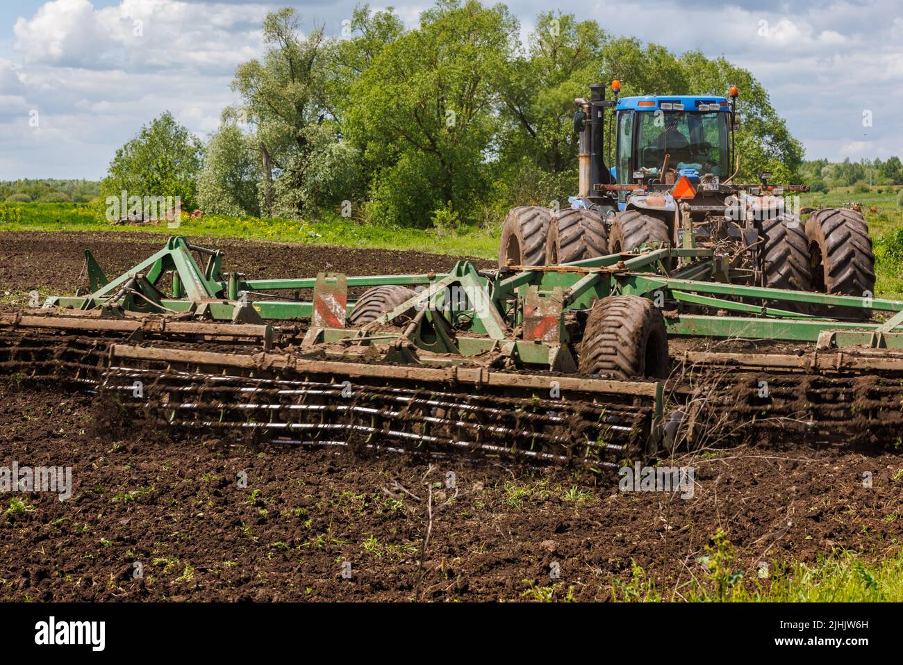 Blue tractor with double wheels pulling disc harrow with roller basket