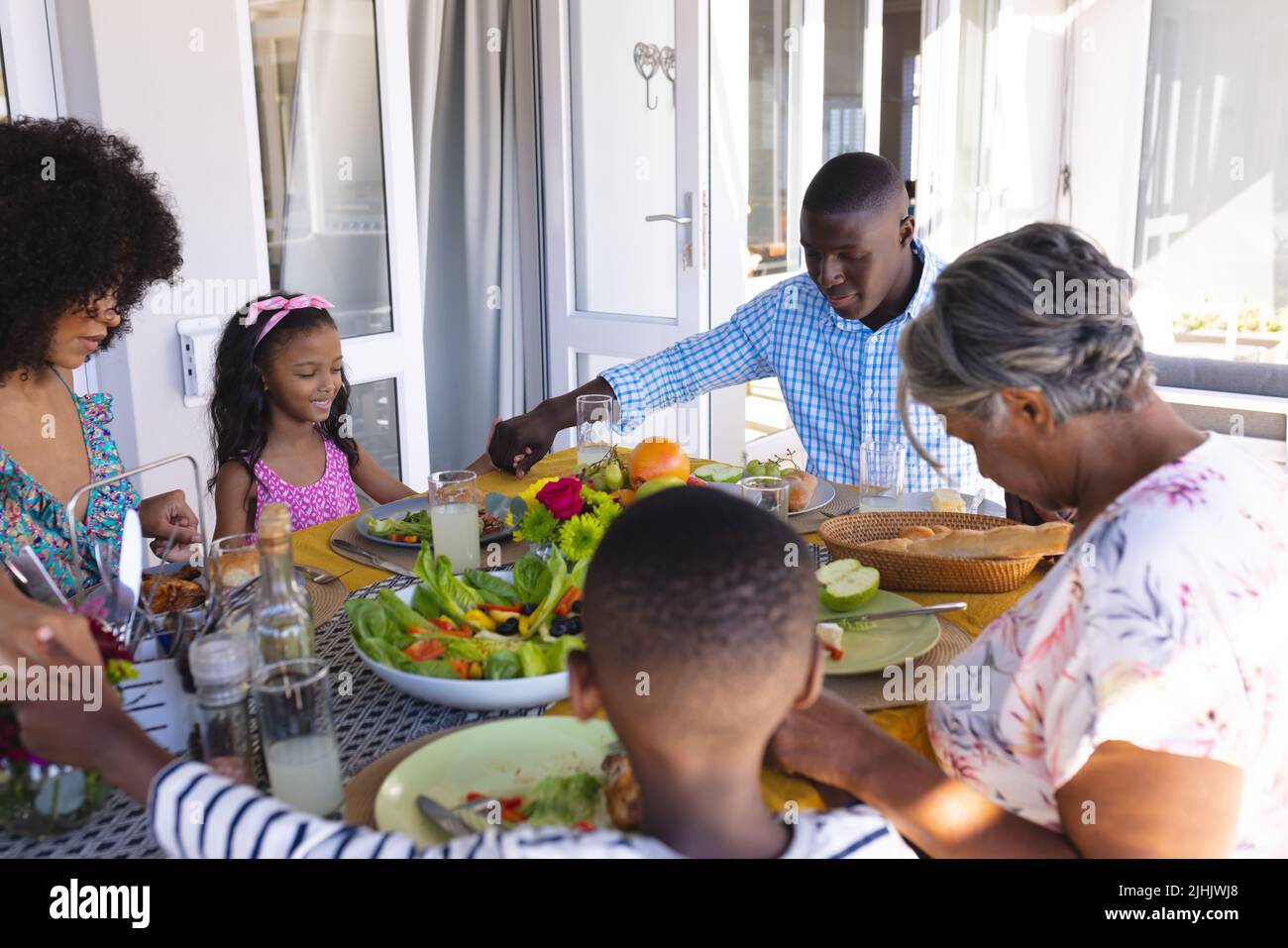 Multiracial multigeneration family holding hands and saying grace before lunch at dining table Stock Photo