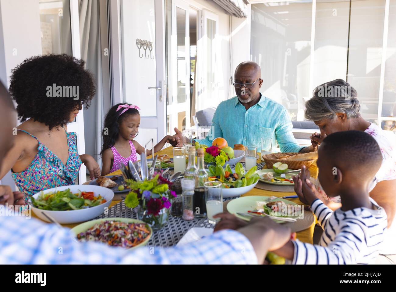 Multiracial multigeneration family holding hands and saying grace at dining table before lunch Stock Photo