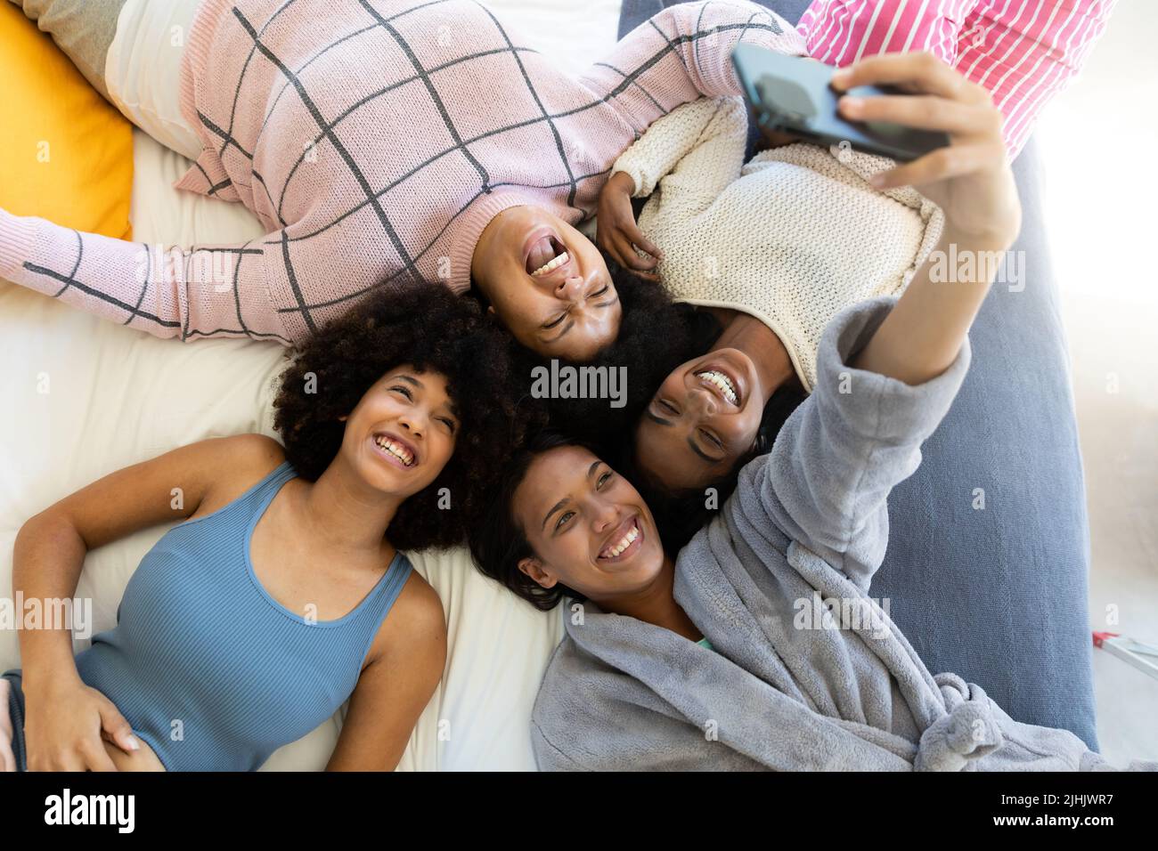High angle view of biracial woman taking selfie over cellphone with cheerful friends lying on bed Stock Photo