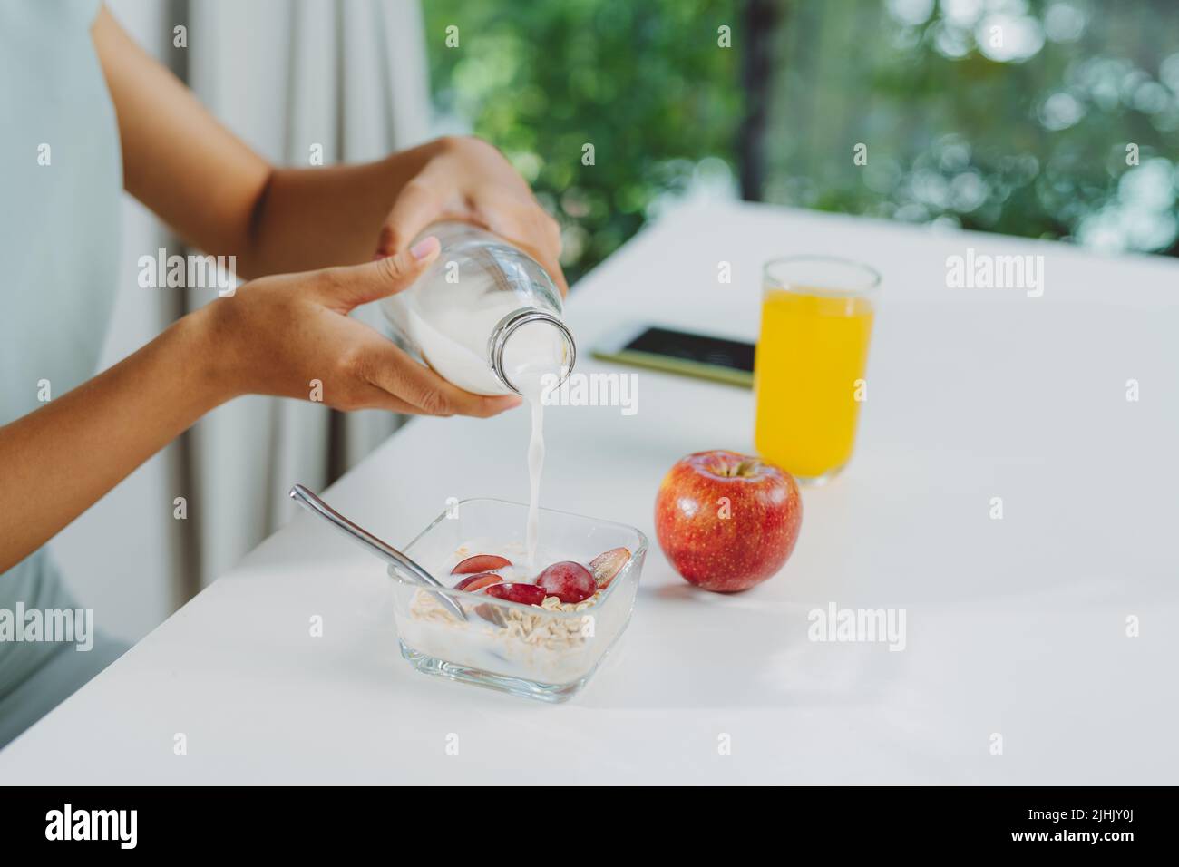 A young woman pours milk into a bowl with granola Stock Photo