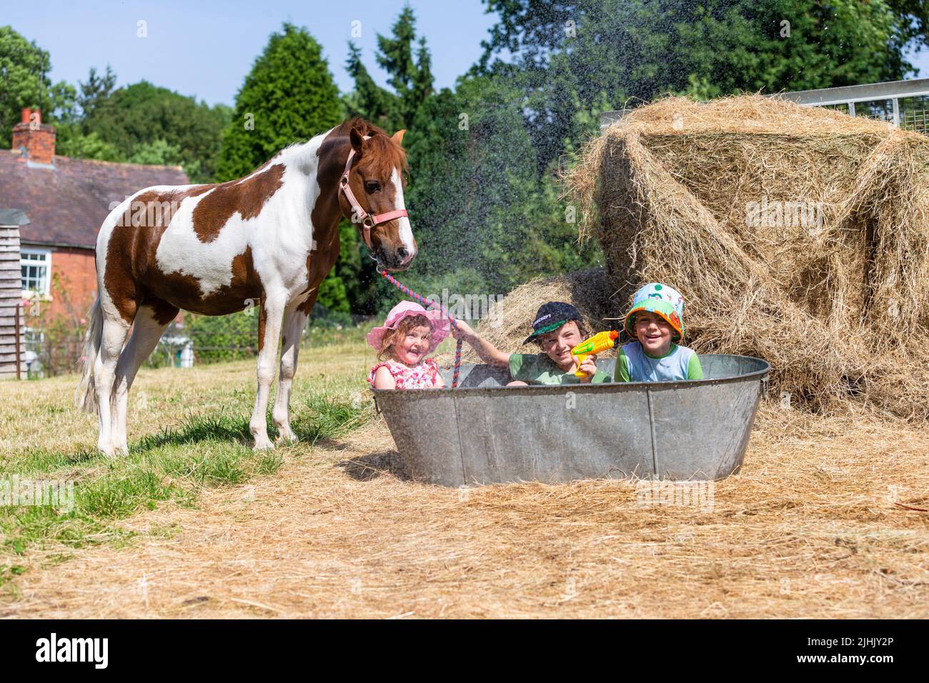 Kidderminster, Worcestershire, UK. 19th July, 2022. Henley Mills, 9, with brother Reggie, 6, and sister Myla-May, 3, have a splashing time in an old tin bath trying to keep cool with their pony Fern in the family's farmyard near Kidderminster, Worcestershire, in a morning where temperatures are set to become UK record highs. Credit: Peter Lopeman/Alamy Live News Stock Photo