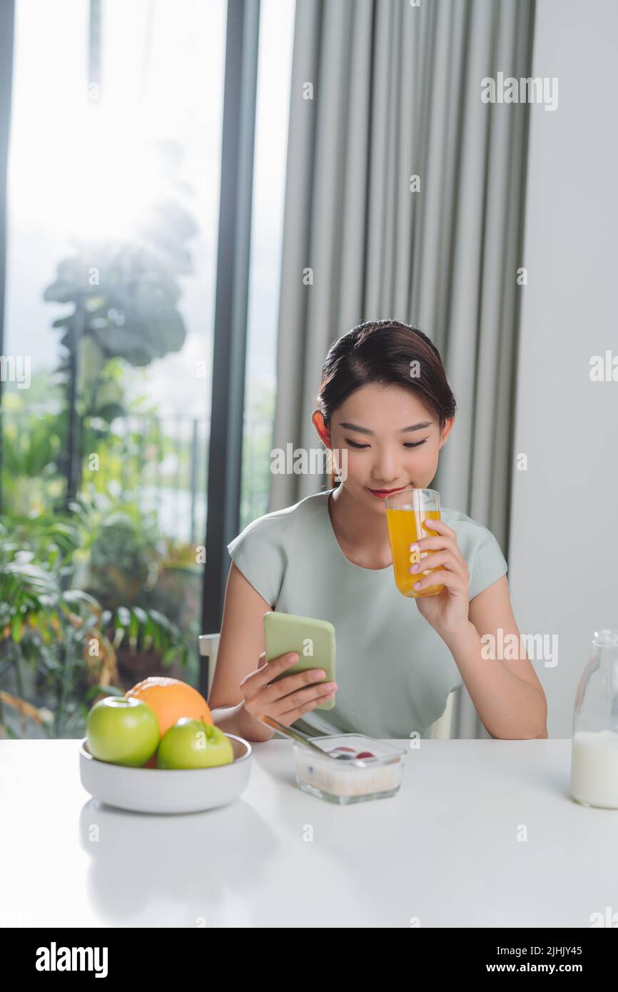 Perfect morning. Happy and positive woman eating breakfast while talking on her smartphone Stock Photo