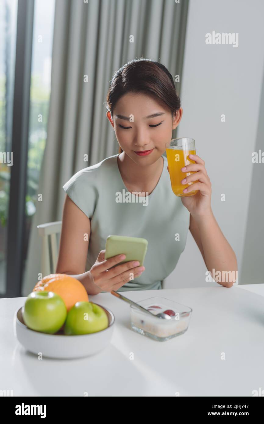 The girl has a healthy breakfast on stylish cozy home at the morning while checking her email on mobile. Stock Photo