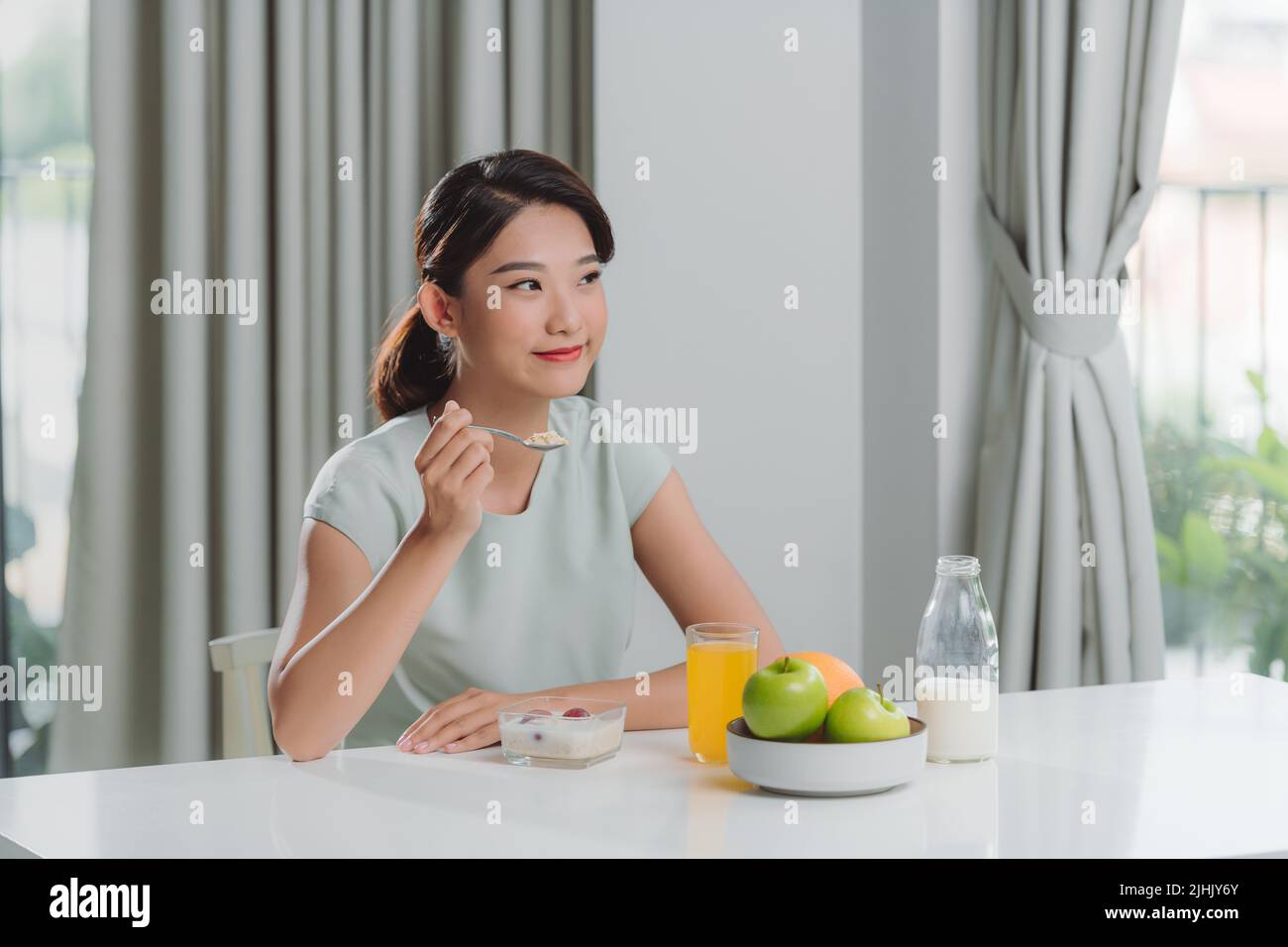 asian young woman having cereals, granola with fresh dairy milk in bowl in kitchen. Stock Photo