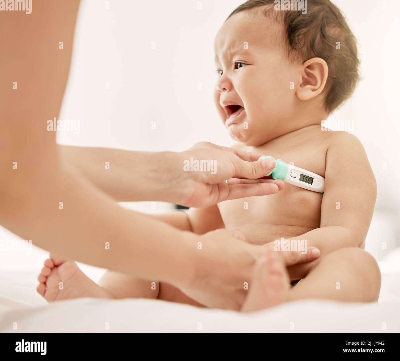 I dont like this, mom. a paediatrician taking a babys temperature with a thermometer. Stock Photo