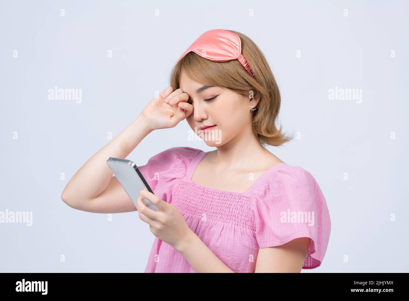 Cheerful girl waking up and grab phone, checking messages, scrolling news feed on smartphone wearing nightwear, sleep mask, smiling Stock Photo