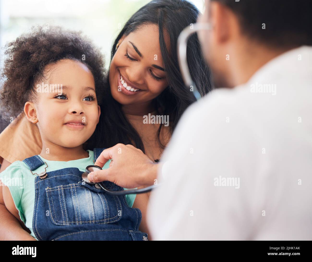 Im a big girl now. a little girl sitting on her mothers lap while being examined by her doctor. Stock Photo