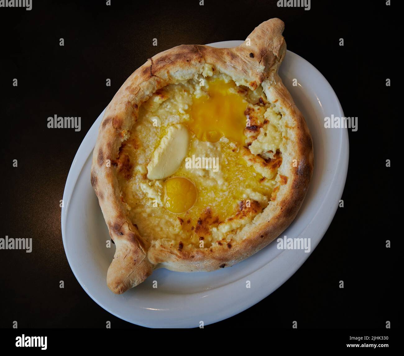 Khachapuri Adjaruli (Georgian Cheese Bread Boat) made with bread, cheese, butter and egg Yolk in a white plate  with black background Stock Photo