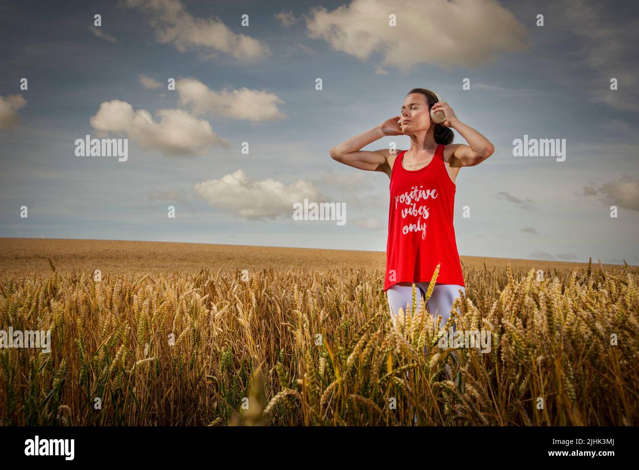 woman standing in a field listening to music on headphones, positive vibes only t shirt. Stock Photo