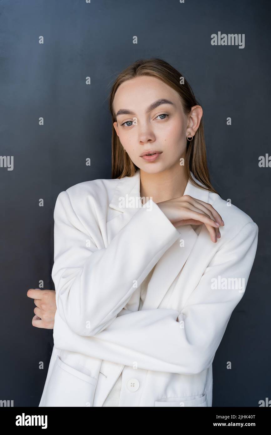 young and sensual woman in white blazer looking at camera on black ...
