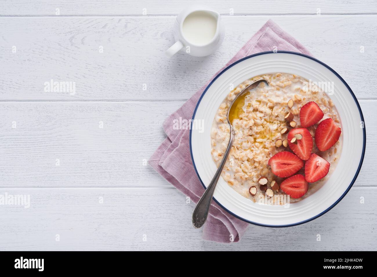 Oatmeal. Bowl of oatmeal porridge with strawberry, almond and milk on white wooden table background. Top view in flat lay style. Natural ingredients. Stock Photo