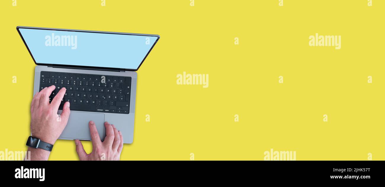 top down view of person using modern laptop computer with copy space on screen against wide yellow background Stock Photo