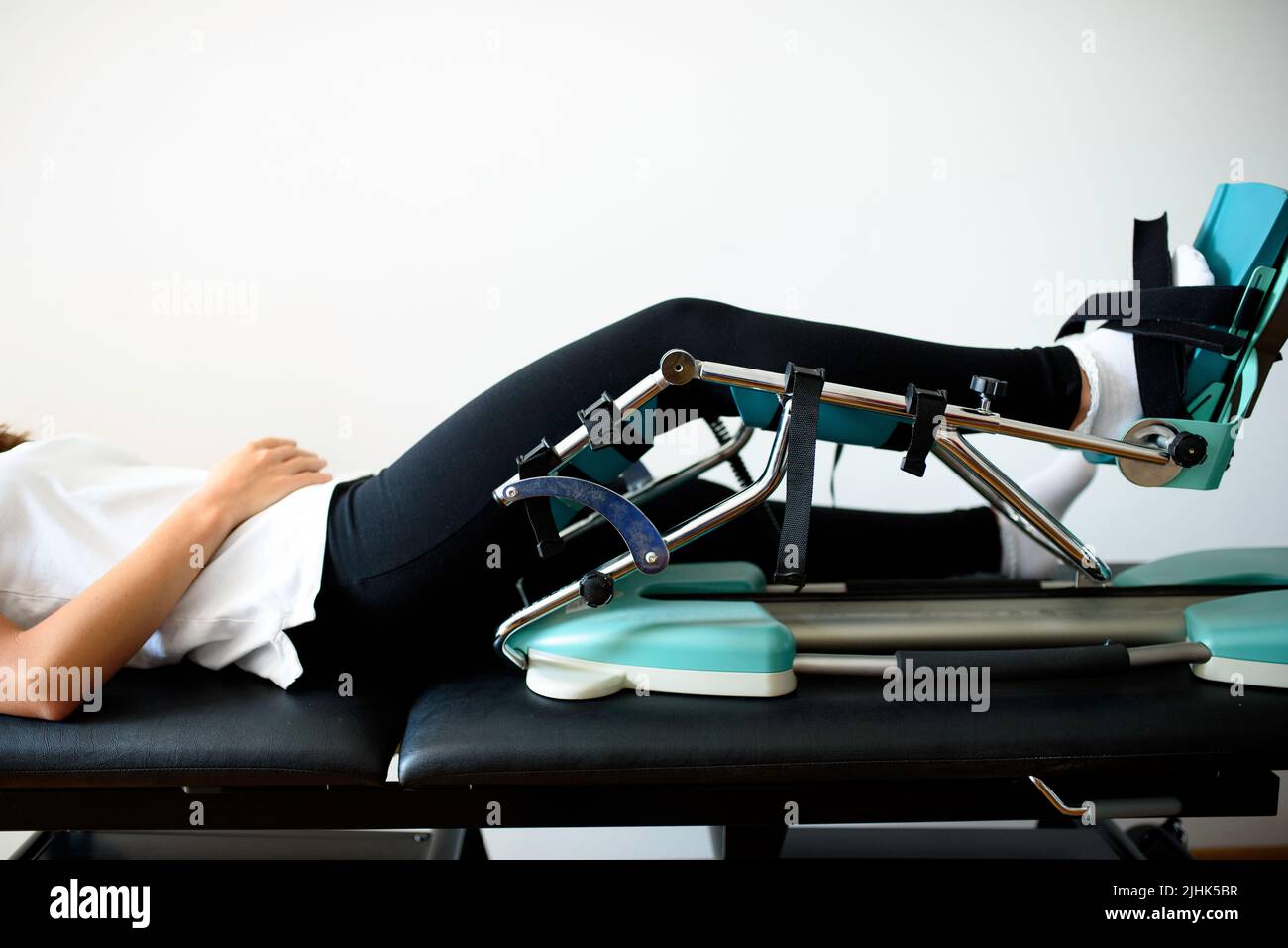 Patient lying on medical leather table with CPM physiotherapy machine and injured knee inside. Passive motion, after surgery machine for knees, hips Stock Photo