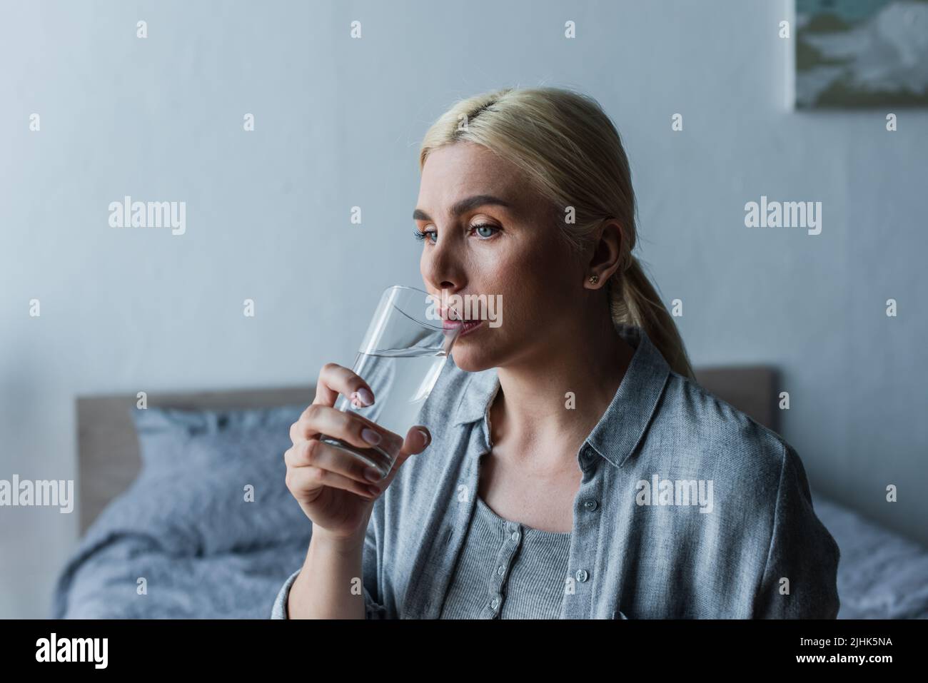 pensive woman with menopause drinking fresh water from glass Stock Photo