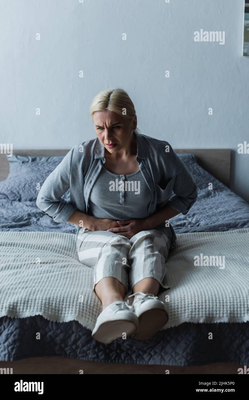 upset blonde woman with menopause suffering from abdominal pain in