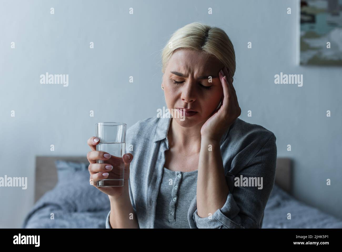 blonde woman with menopause suffering from headache and holding glass of water Stock Photo