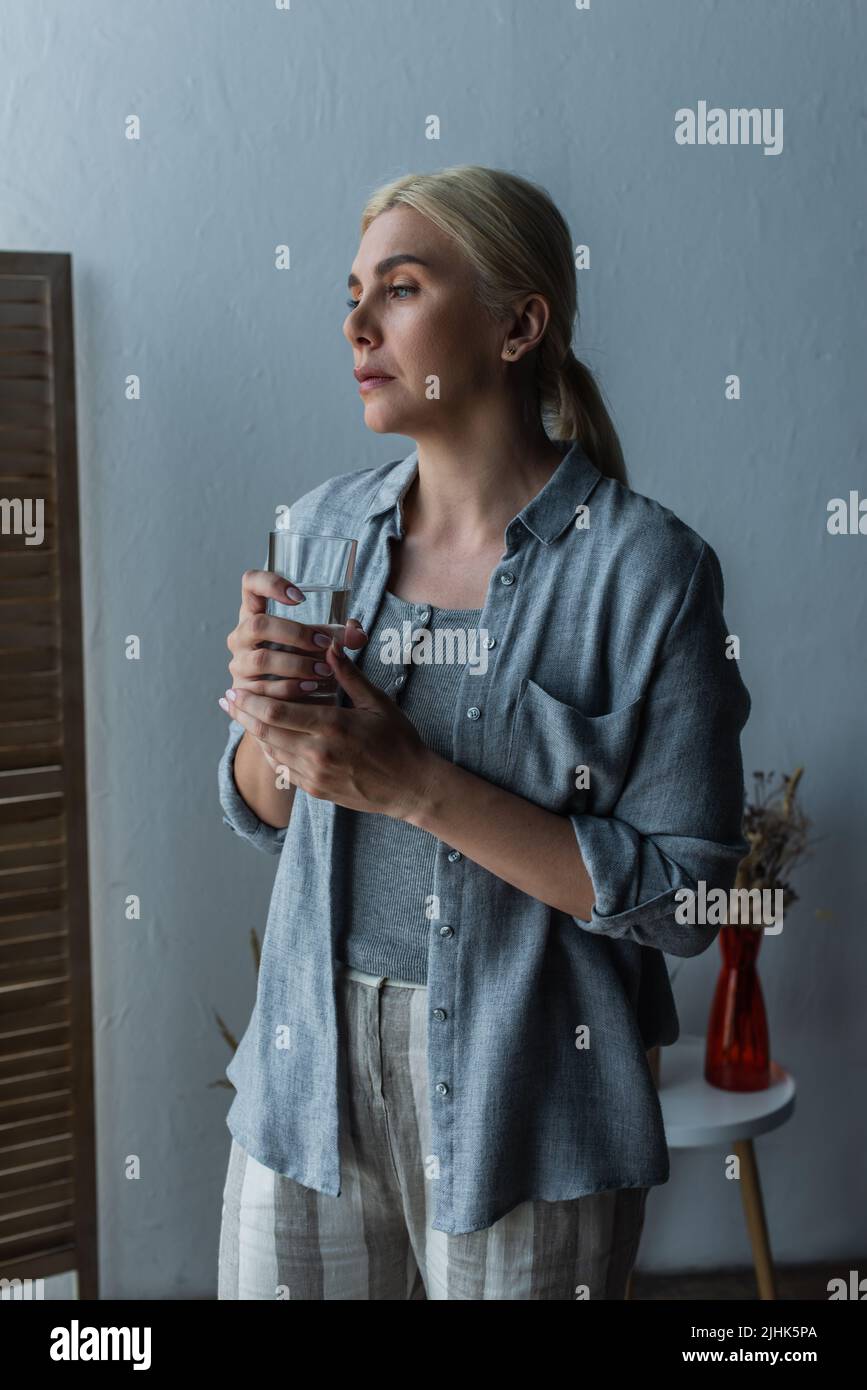 blonde woman with menopause holding glass of water and looking away Stock Photo