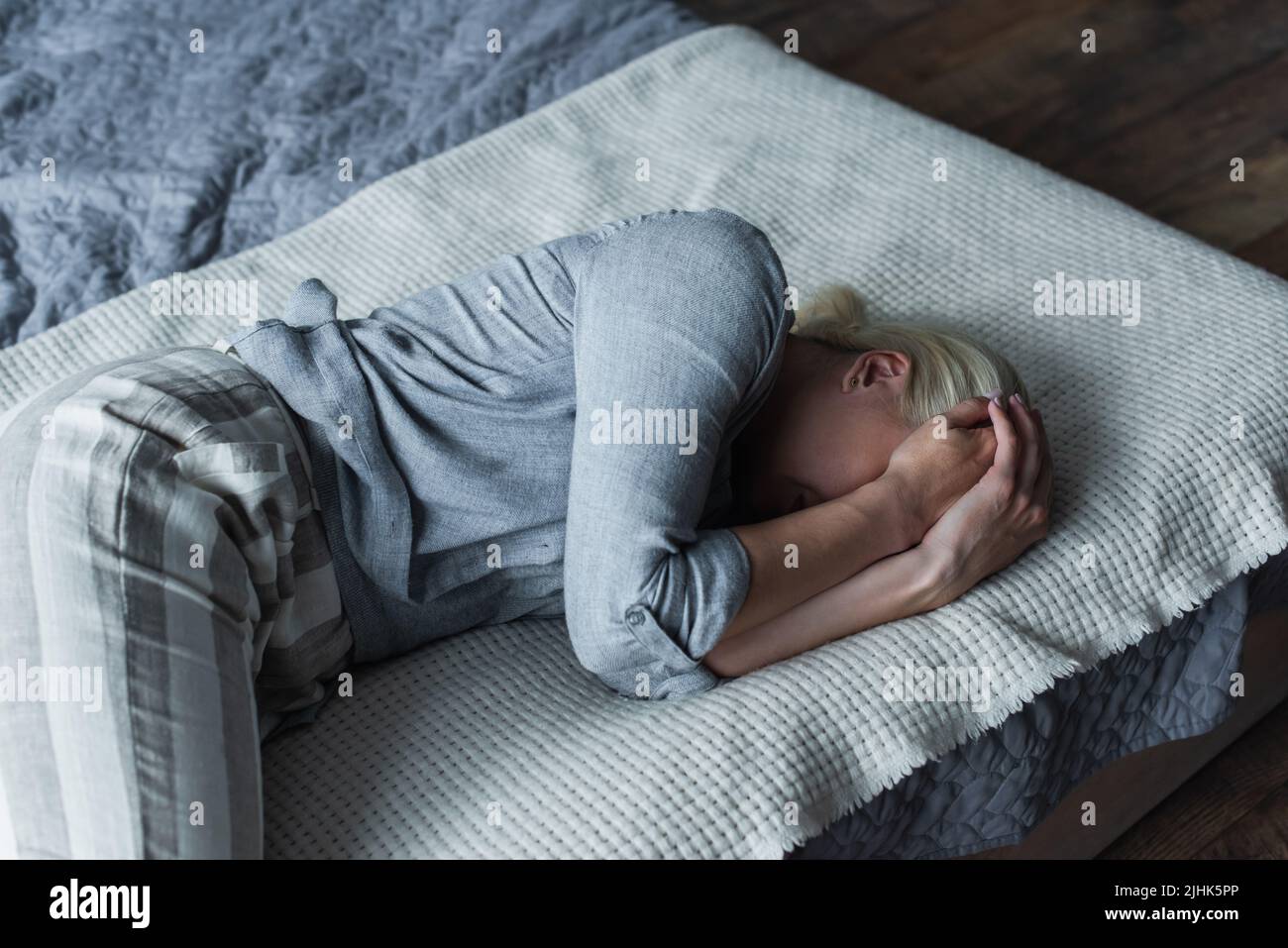 blonde woman lying on bed and covering face while suffering from