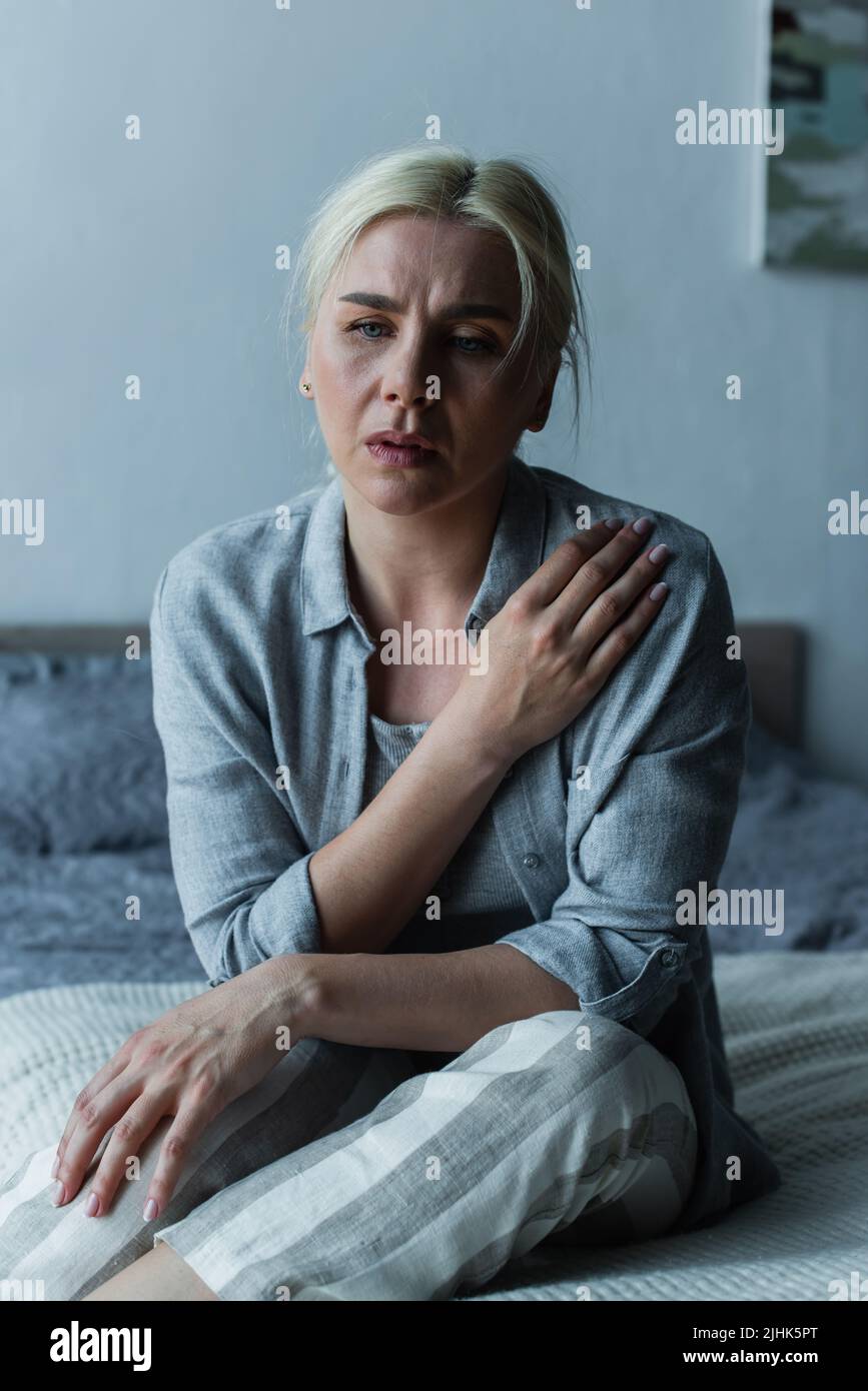 exhausted blonde woman sitting in bedroom during menopause Stock Photo