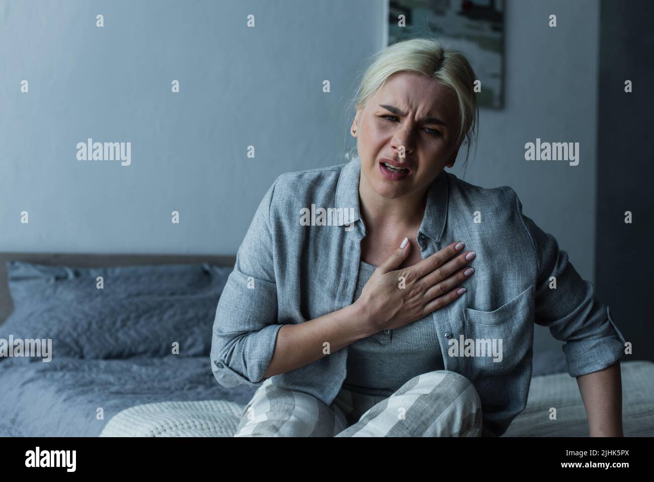 exhausted blonde woman touching chest and feeling pain during menopause