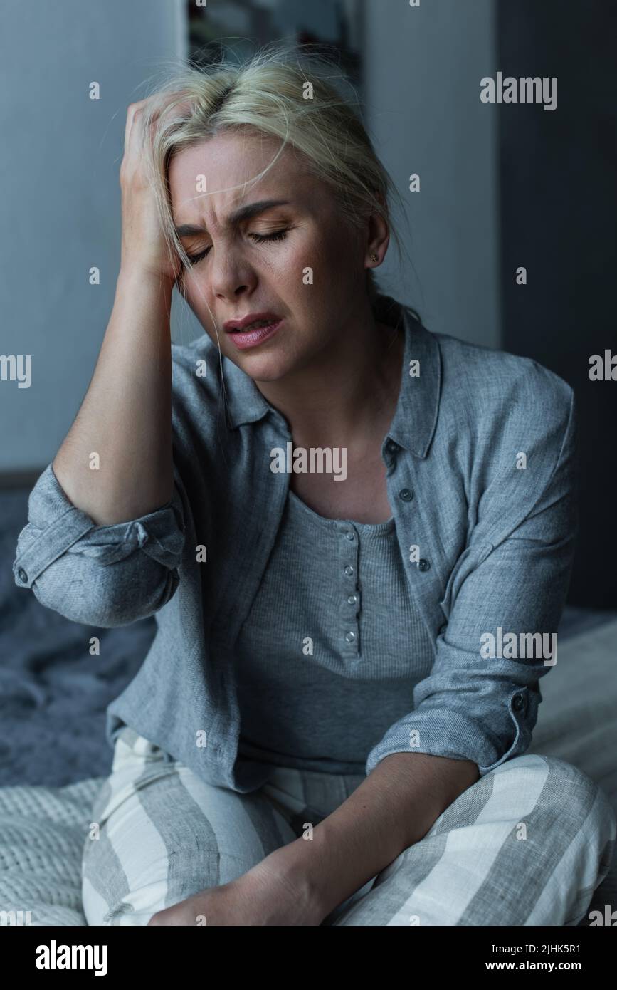 exhausted blonde woman touching head and having migraine during