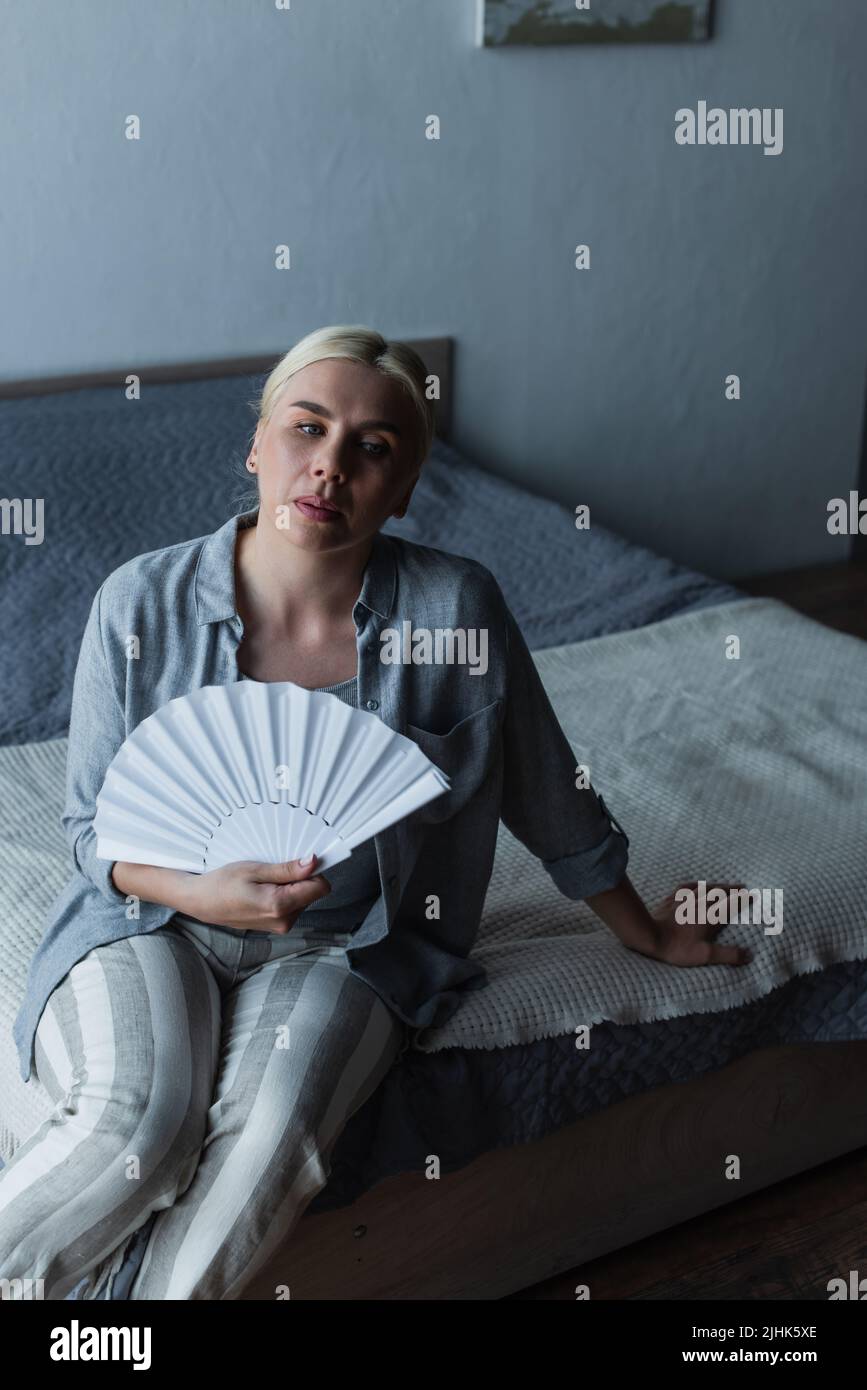 blonde woman with menopause suffering from heat and cooling with fan in