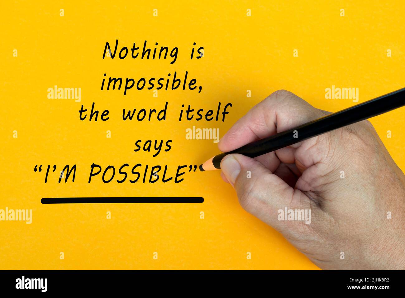 Male hand writes in black pencil the word NOTHING IS IMPOSSIBLE, THE WORD ITSELF SAYS I AM POSSIBLE on a yellow background. Stock Photo
