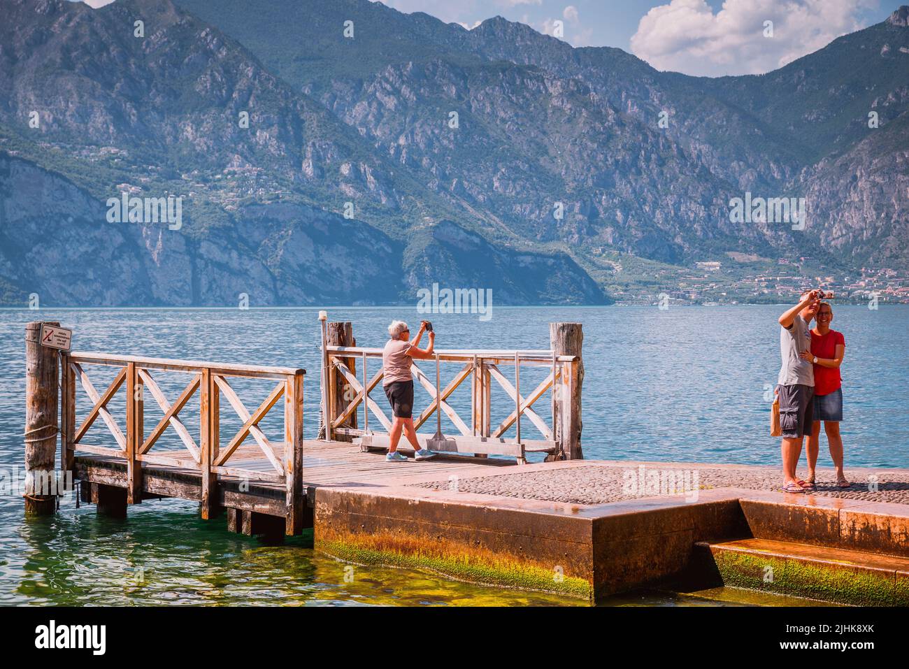 Tourists next to Lake Garda on a wooden pier. Malcesine is a comune, municipality, on the eastern shore of Lake Garda in the Province of Verona in the Stock Photo