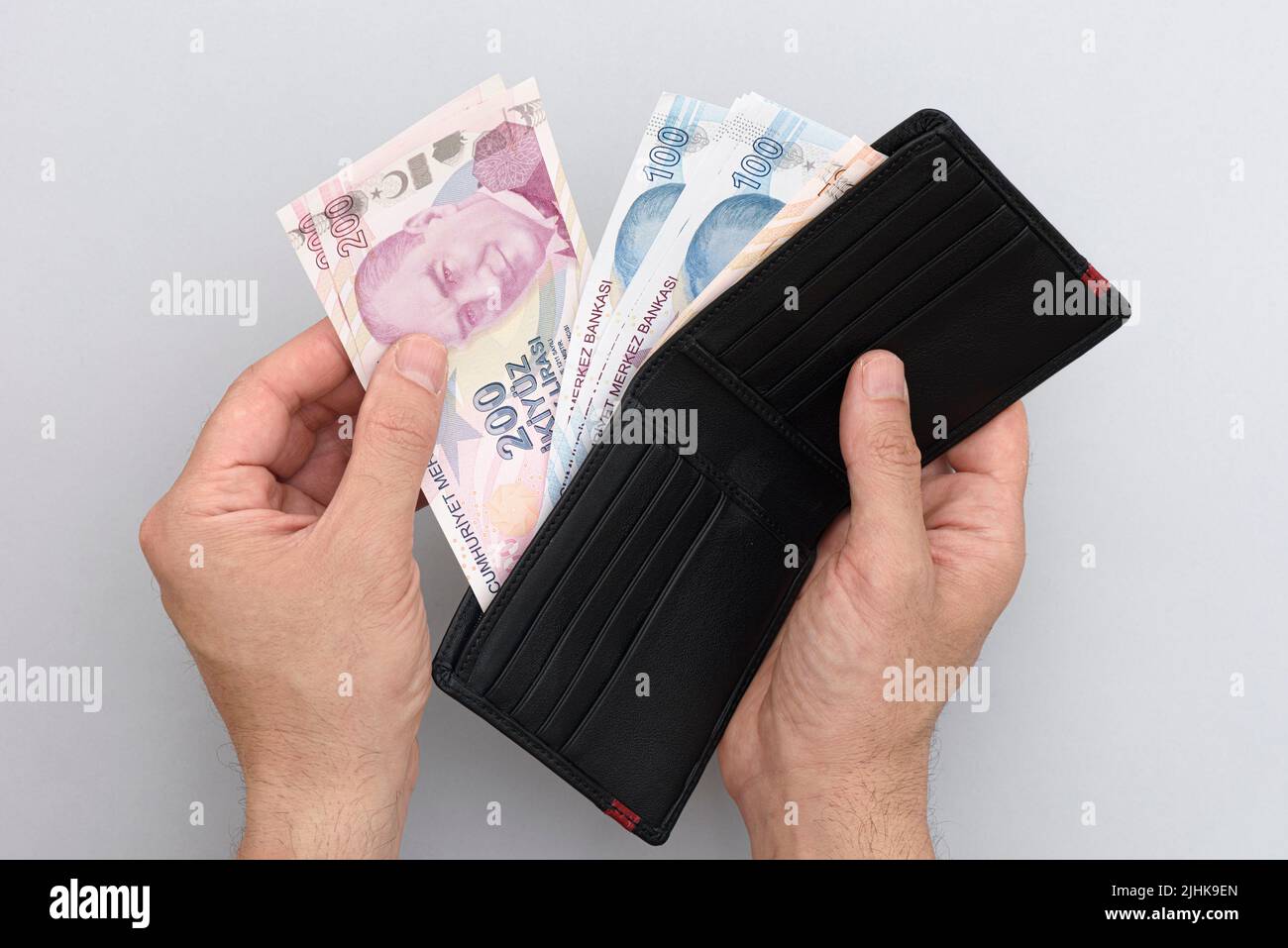 Male hand holding wallet with Turkish lira banknotes. Gray background