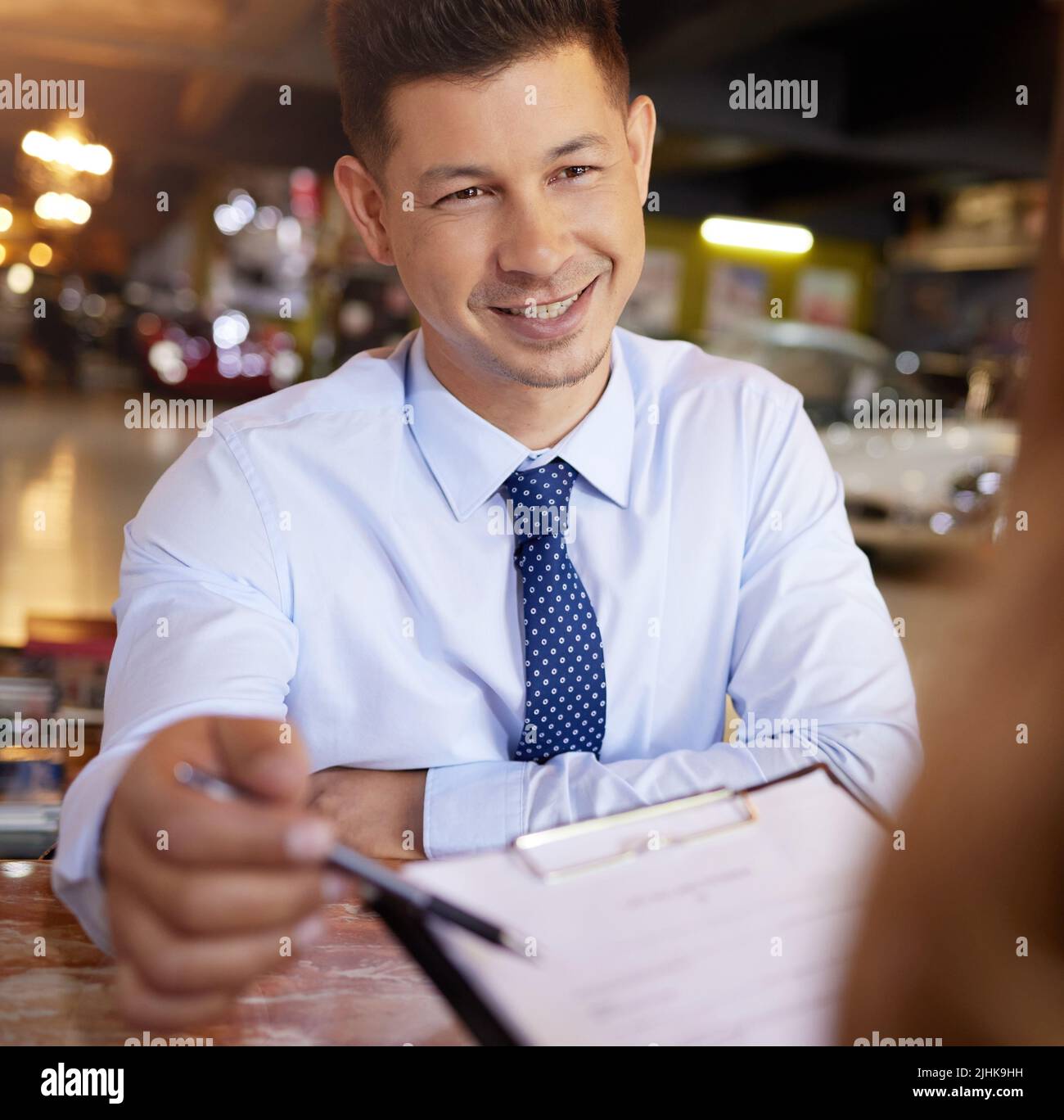 Just initial here.... a handsome mature male car salesman talking to a customer in his office at the car dealership. Stock Photo