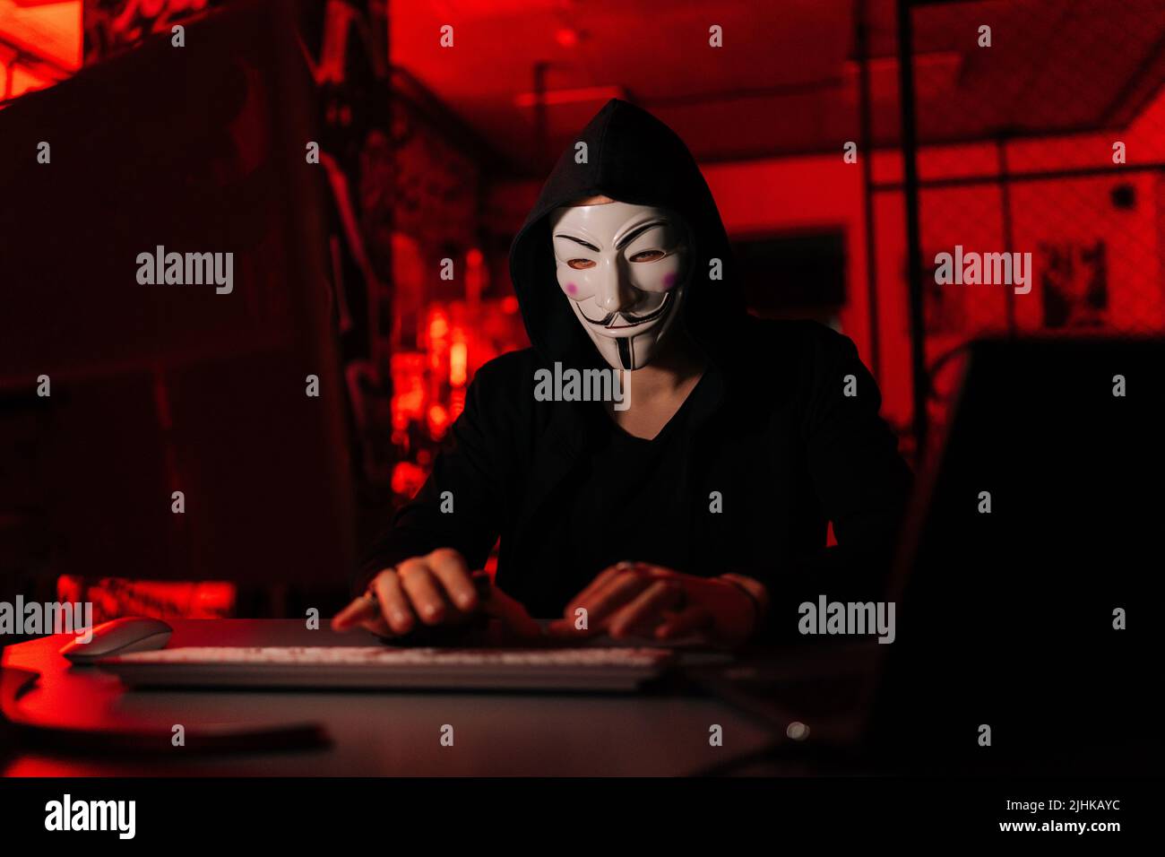 Portrait of dangerous unrecognizable hacker man wearing anonymous mask starting breaking computer system and typing password for hacking bank account. Stock Photo