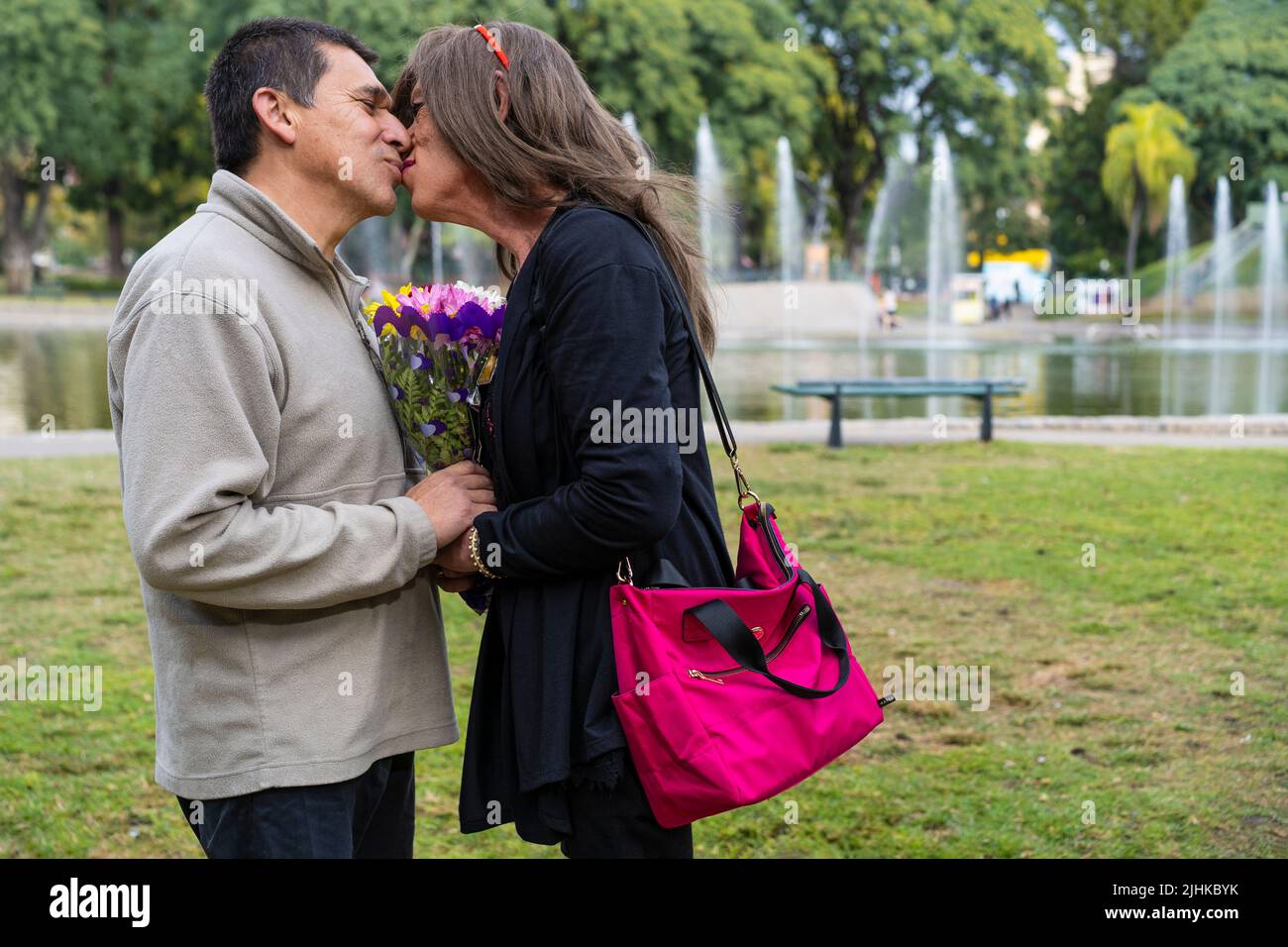 Mature trans woman kissing her boyfriend in a park happy because he gave her flowers Stock Photo