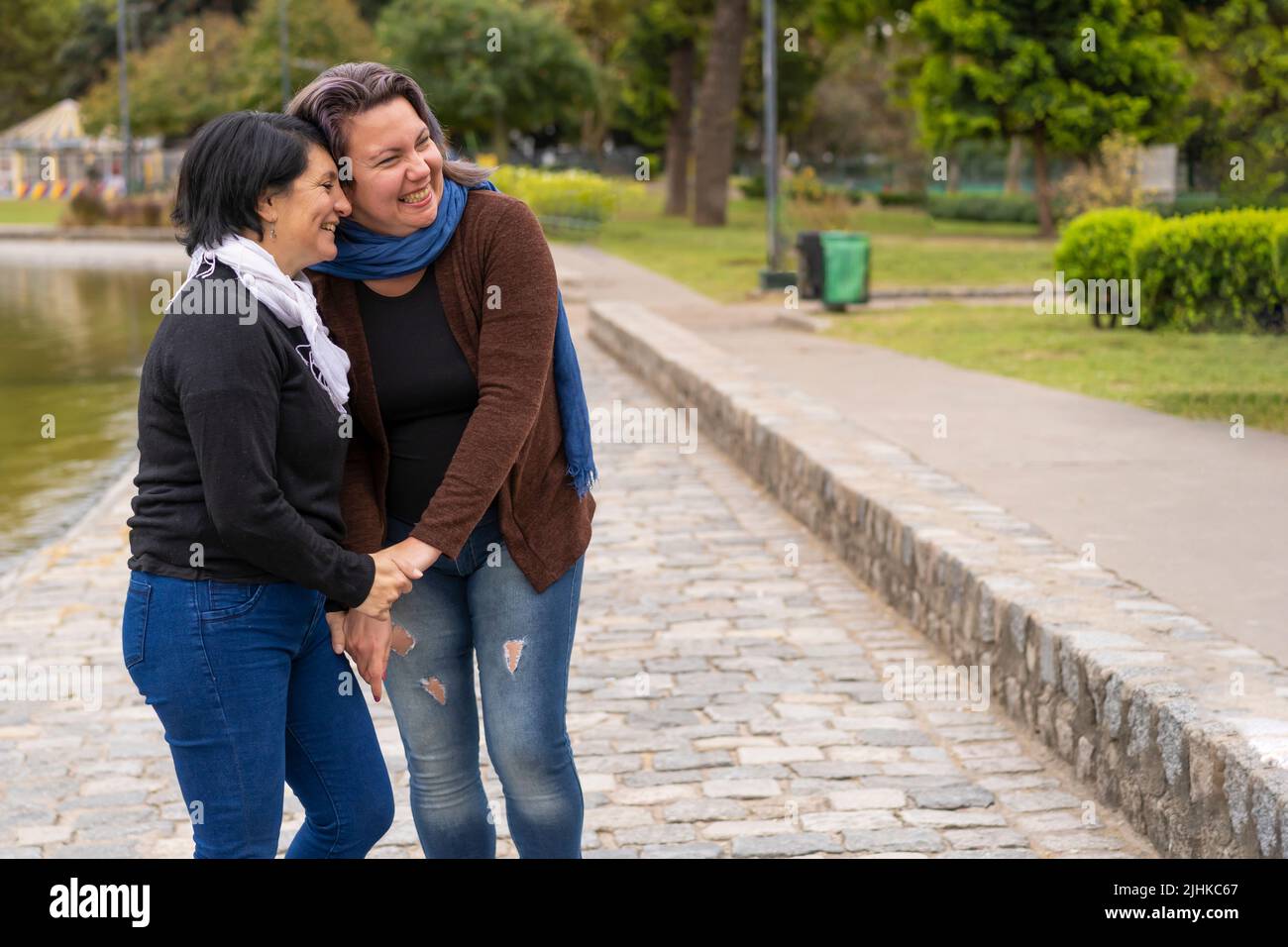 Lesbian couple in a park holding hands laughing. Copy space Stock Photo