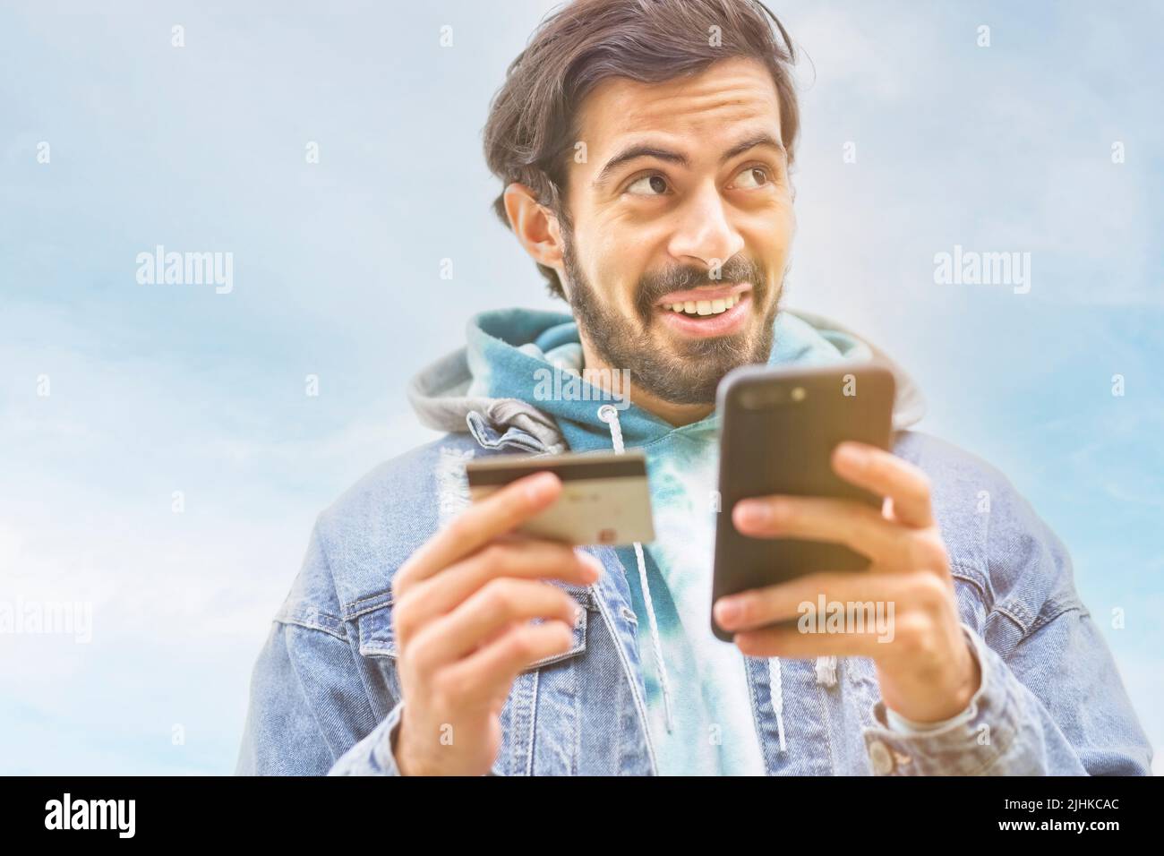 Latin man using credit card to make online payment on smartphone. Mixed race man using cellphone for shopping online. Guy using smart phone to check c Stock Photo