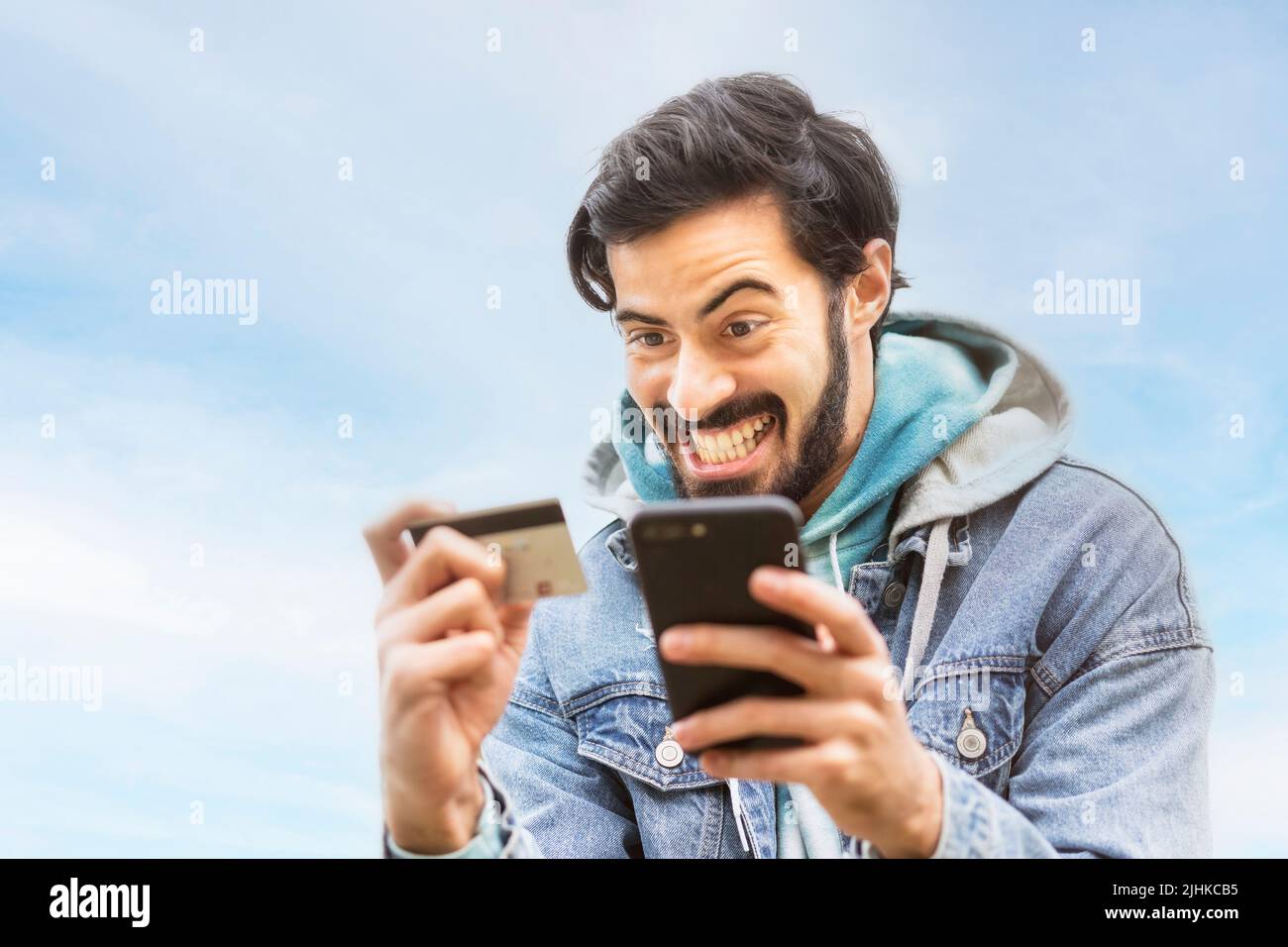 Latin man using credit card to make online payment on smartphone. Mixed race man using cellphone for shopping online. Guy using smart phone to check c Stock Photo
