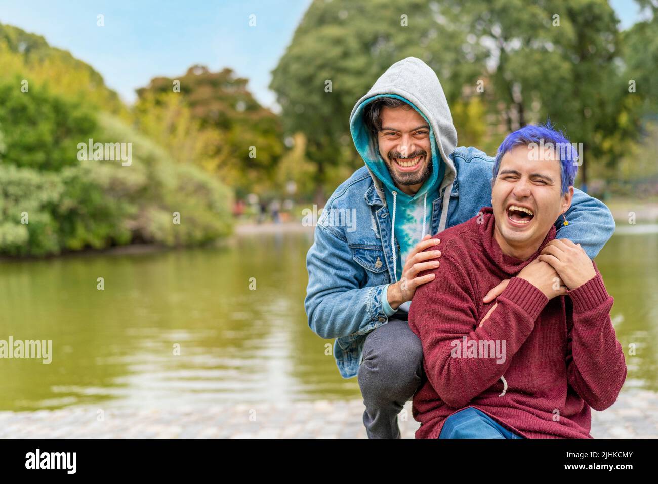 Gay Latino male couple sitting on a bench in a park laughing Stock Photo