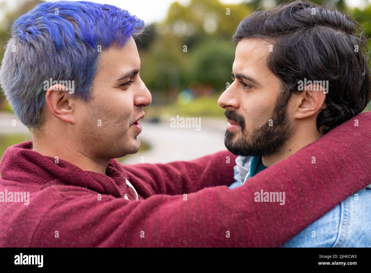 Latin gay couple hugging in a park looking at each other about to kiss Stock Photo