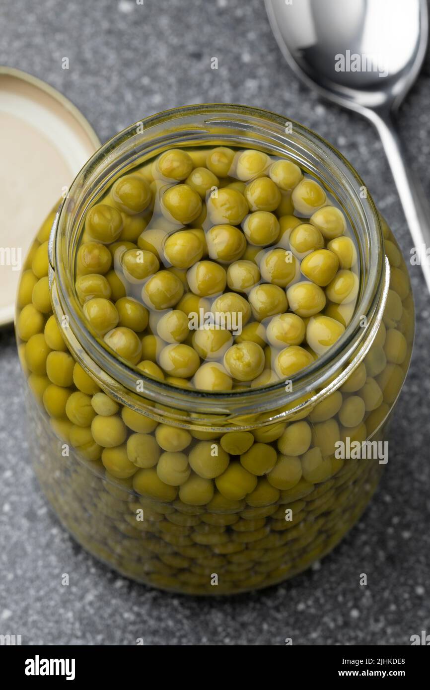 Open glass jar with small green peas close up Stock Photo