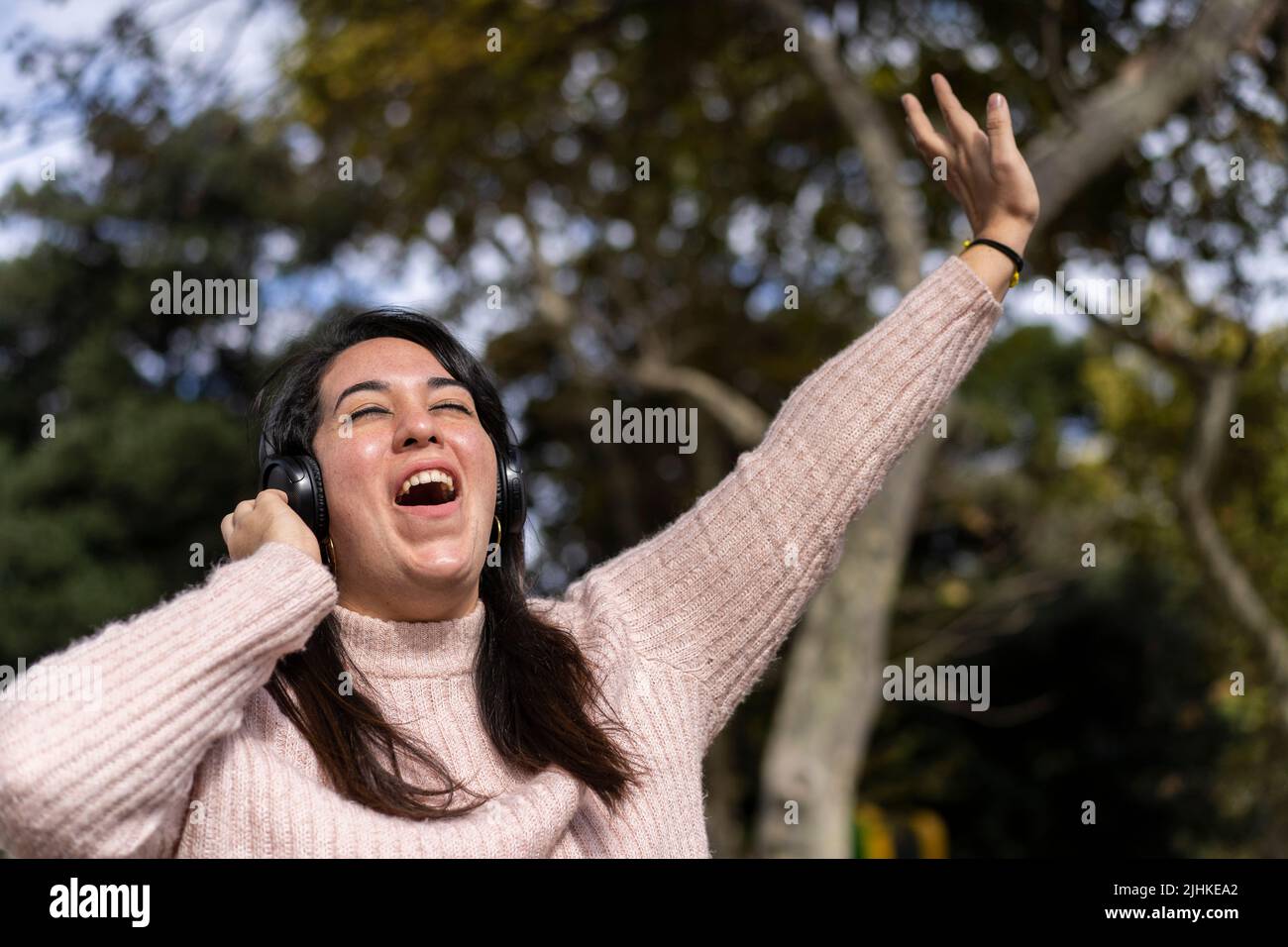 Young latin woman listening to music outdoors with headphones. Expression of happiness, winning attitude. Copy space Stock Photo