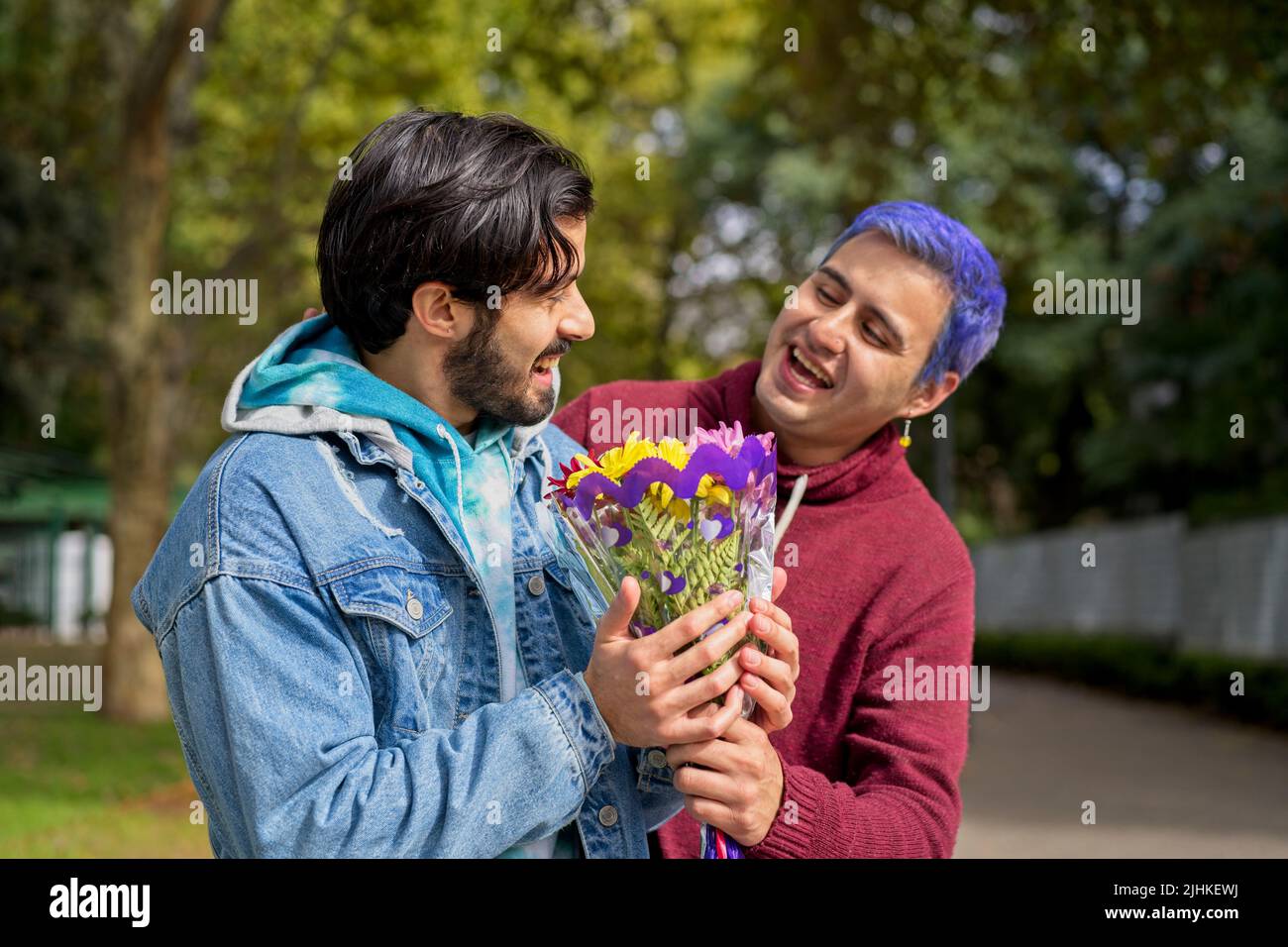 Couple of Latino gay men in a park embracing each other. One surprising the other with a bouquet of flowers as a gift Stock Photo