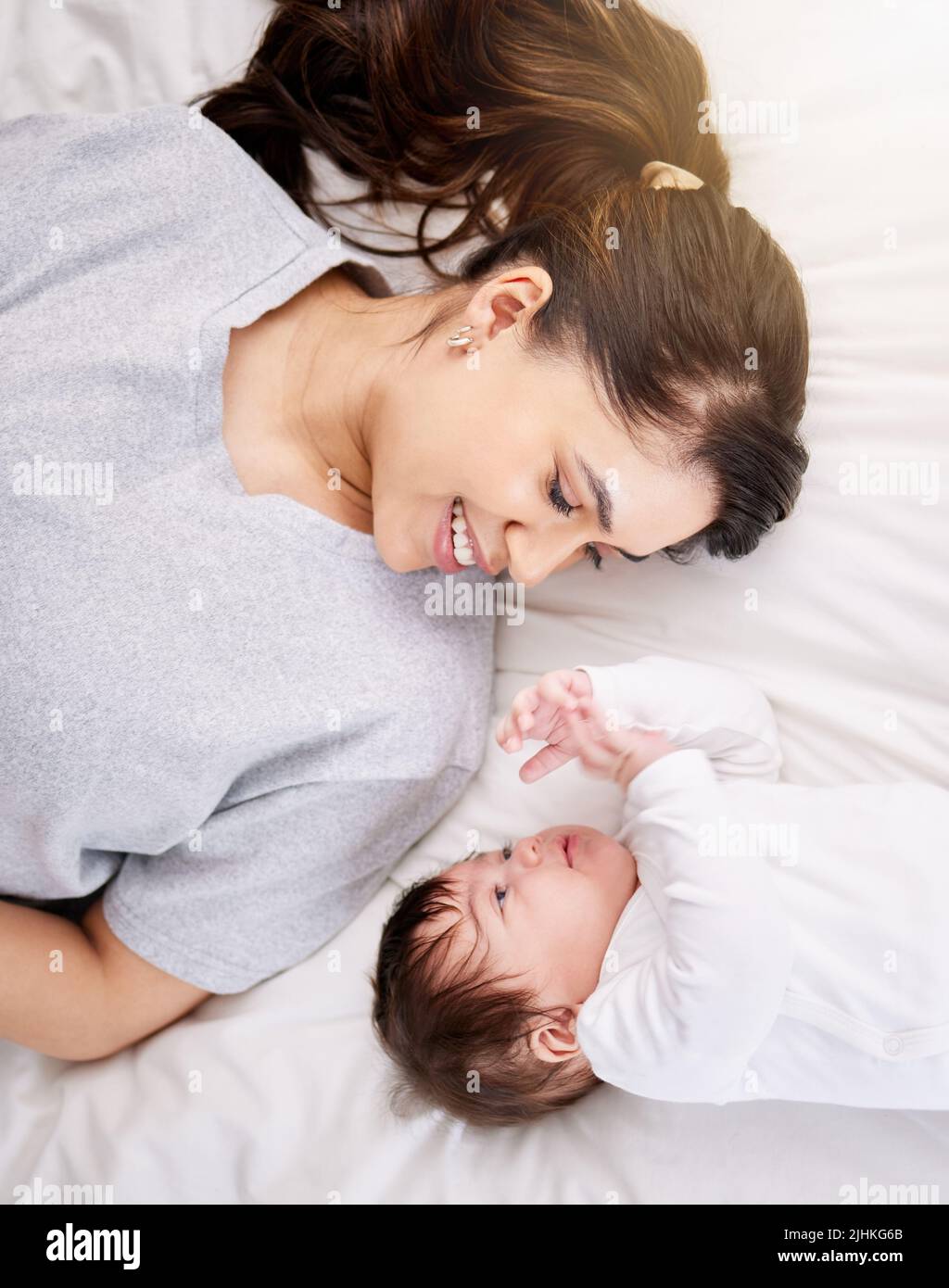 A single mixed race hispanic woman bonding with her newborn baby while talking in bed and having fun. Hispanic woman enjoying being a mother while Stock Photo