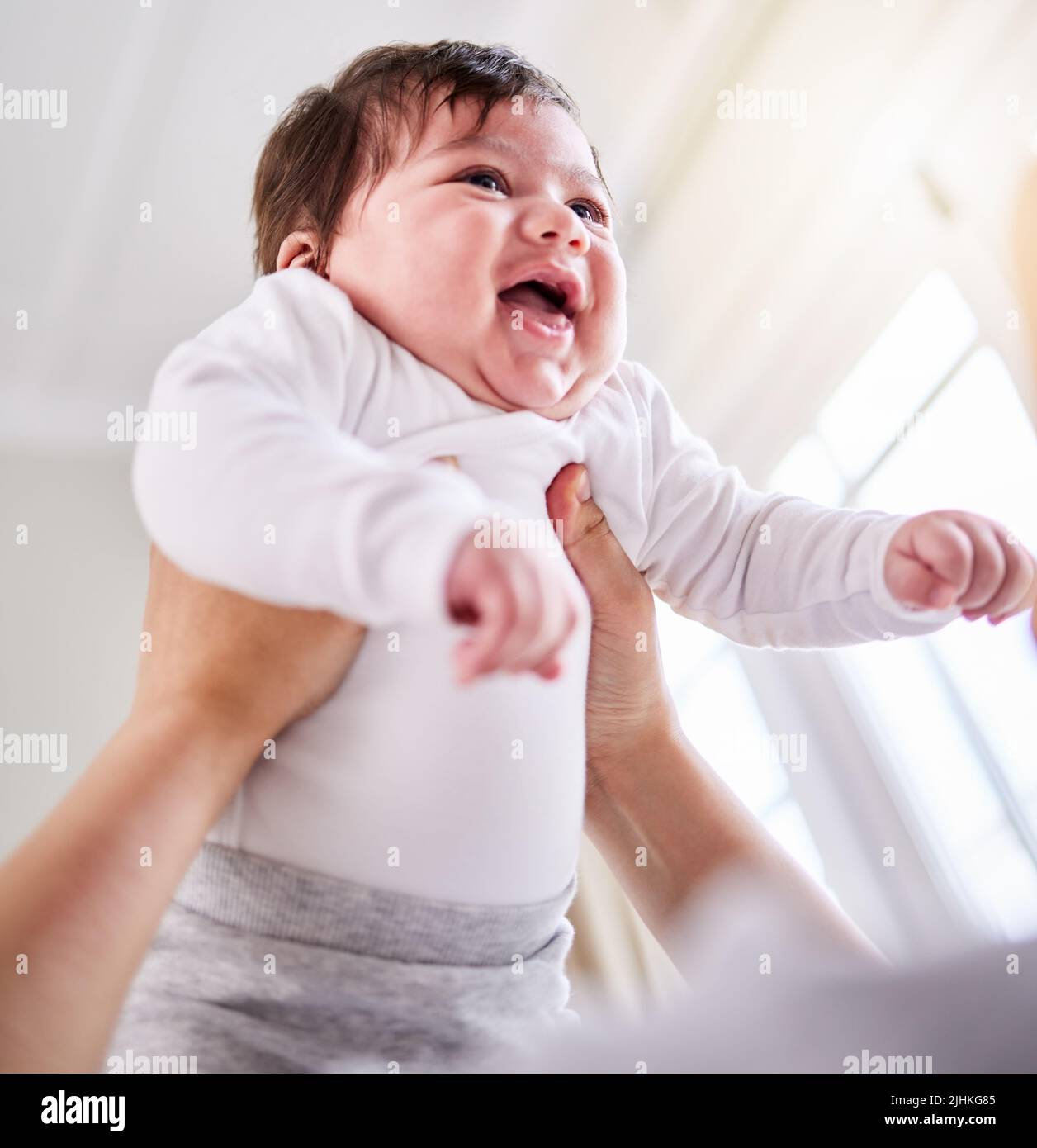 a mixed race adorable cute little baby laughing. Young mother playing with her newborn baby while laughing and enjoying bonding with her infant at Stock Photo