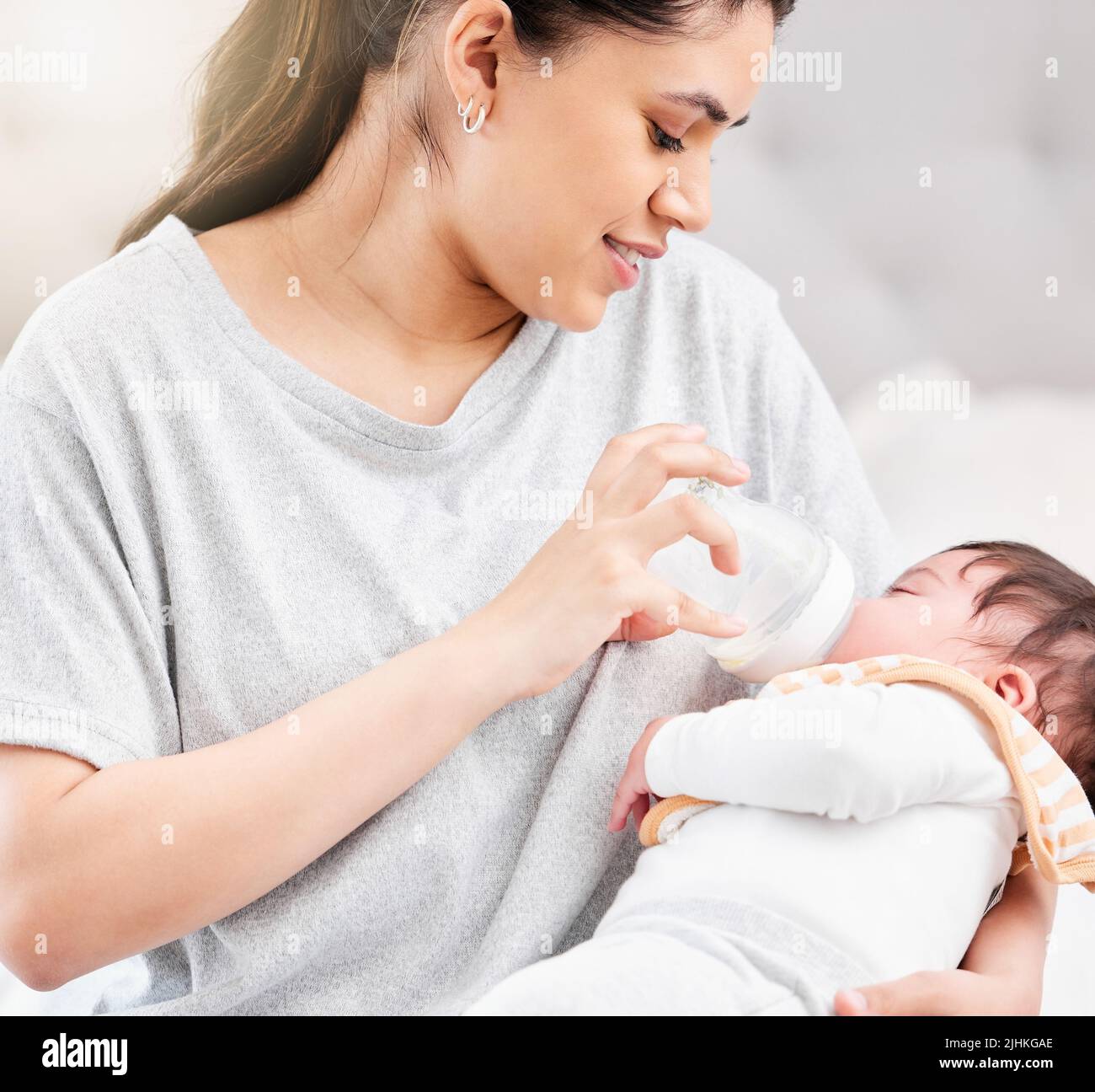 Young hispanic mother feeding her newborn baby a milk bottle and bonding with her. Little baby asleep in her mothers arms in her bedroom. Small, tiny Stock Photo