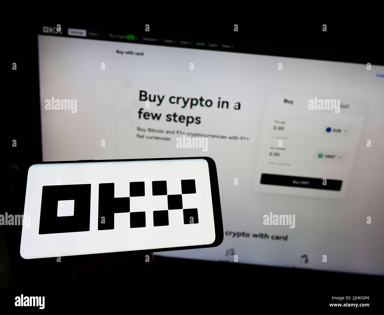 Person holding smartphone with logo of crypto company Aux Cayes FinTech Co. Ltd. (OKX) on screen in front of website. Focus on phone display. Stock Photo