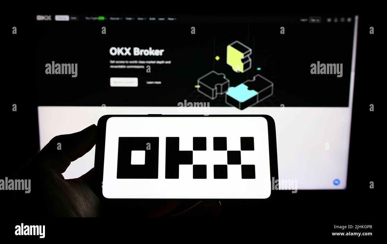 Person holding cellphone with logo of crypto company Aux Cayes FinTech Co. Ltd. (OKX) on screen in front of webpage. Focus on phone display. Stock Photo
