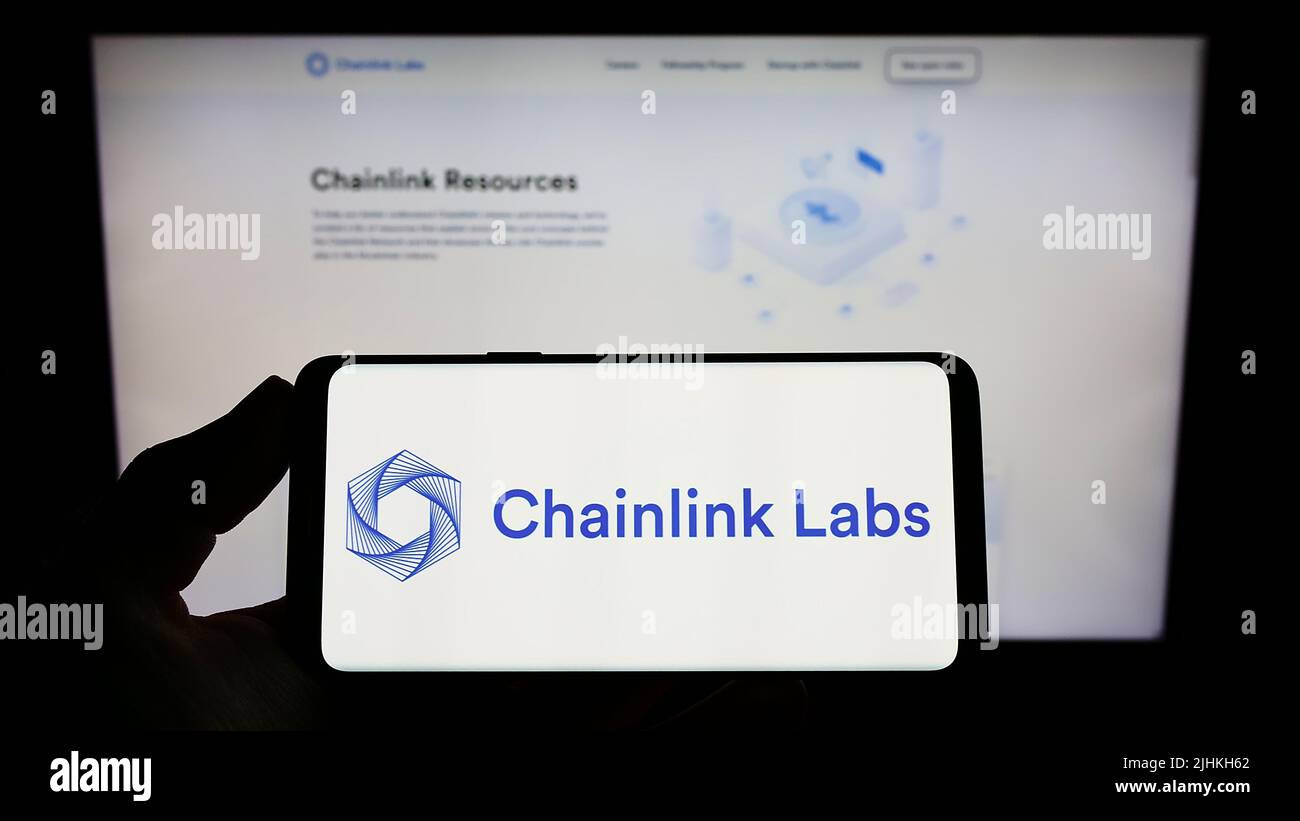 Person holding smartphone with logo of US blockchain company Chainlink Labs on screen in front of website. Focus on phone display. Stock Photo