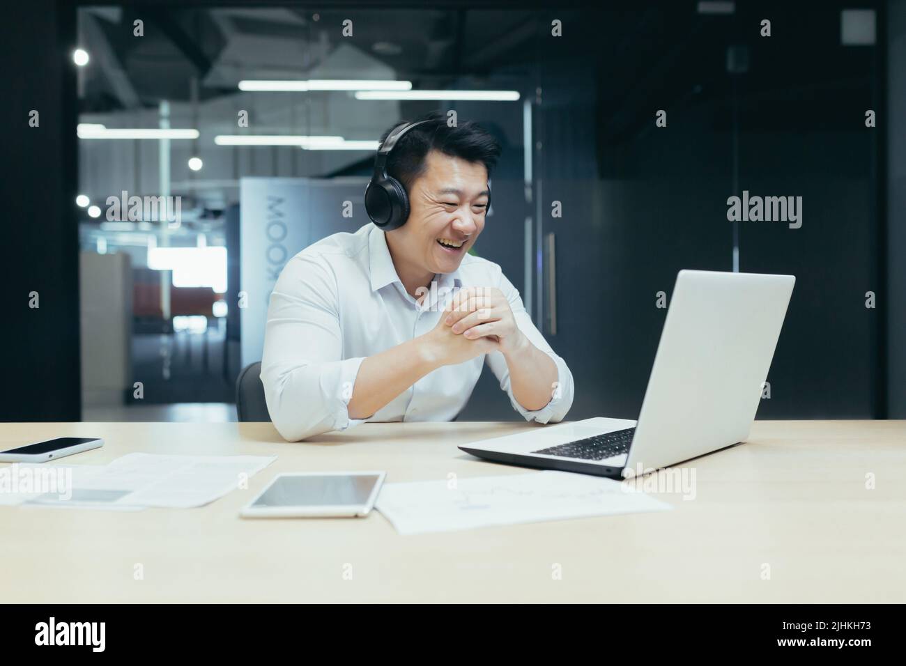 Happy Asian businessman watching sports match online, man in office looking at laptop screen cheerfully cheering Stock Photo