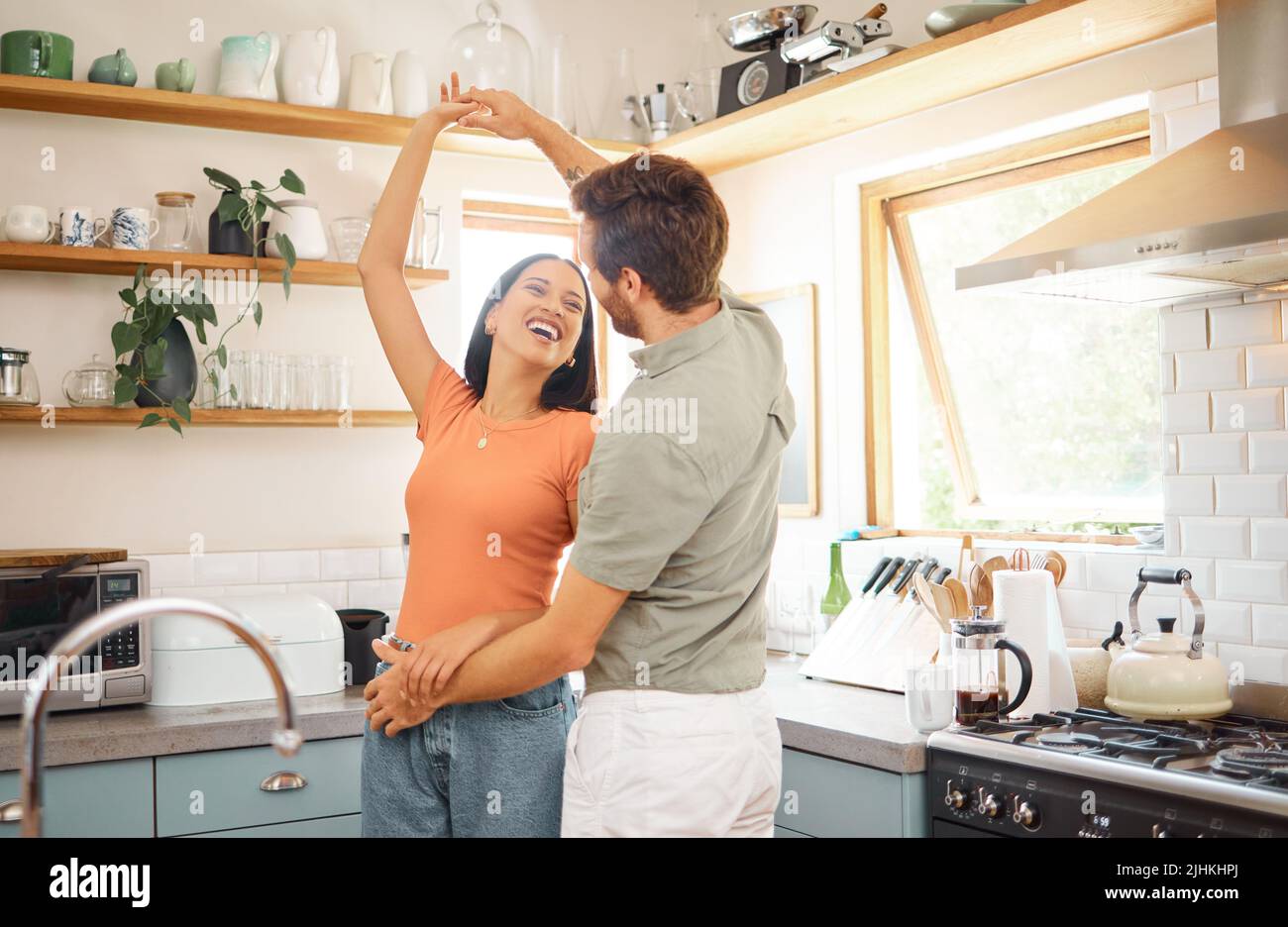 Young content interracial couple dancing in the kitchen at home. Playful caucasian boyfriend and mixed race girlfriend having fun. Happy husband and Stock Photo
