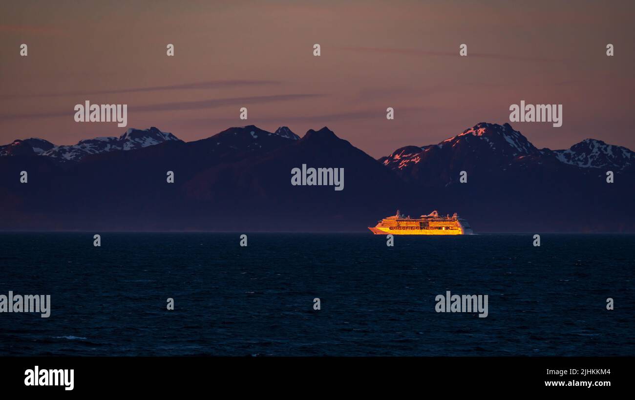 Late evening sunset illuminates a very distant cruise ship against the snowy Alaska coastline Stock Photo